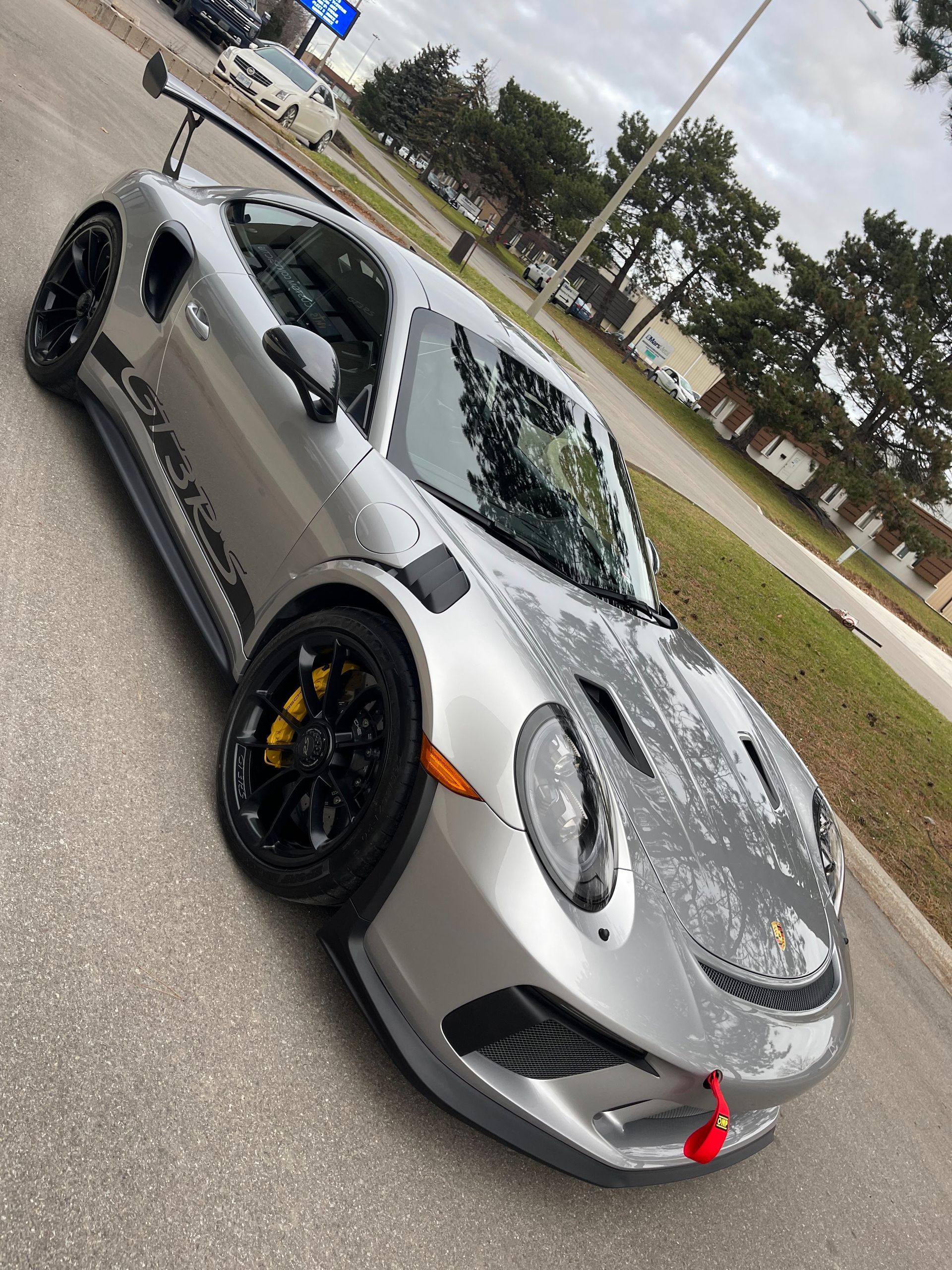 A silver Porsche 911 GT3 RS parked outdoors on asphalt, featuring black wheels, yellow brake calipers, and a rear wing.