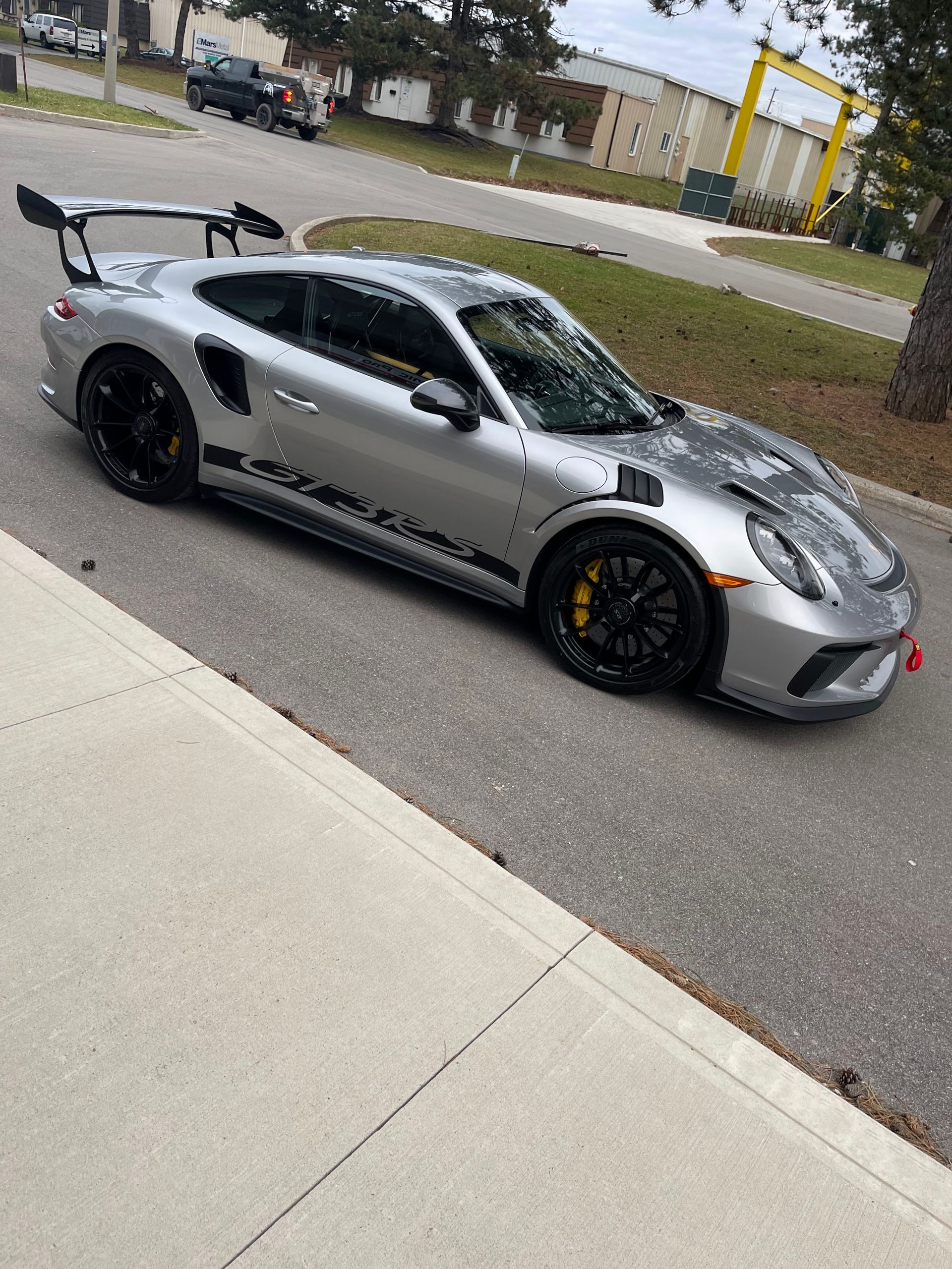 A silver Porsche 911 GT3 RS parked on an asphalt street, viewed from the side.