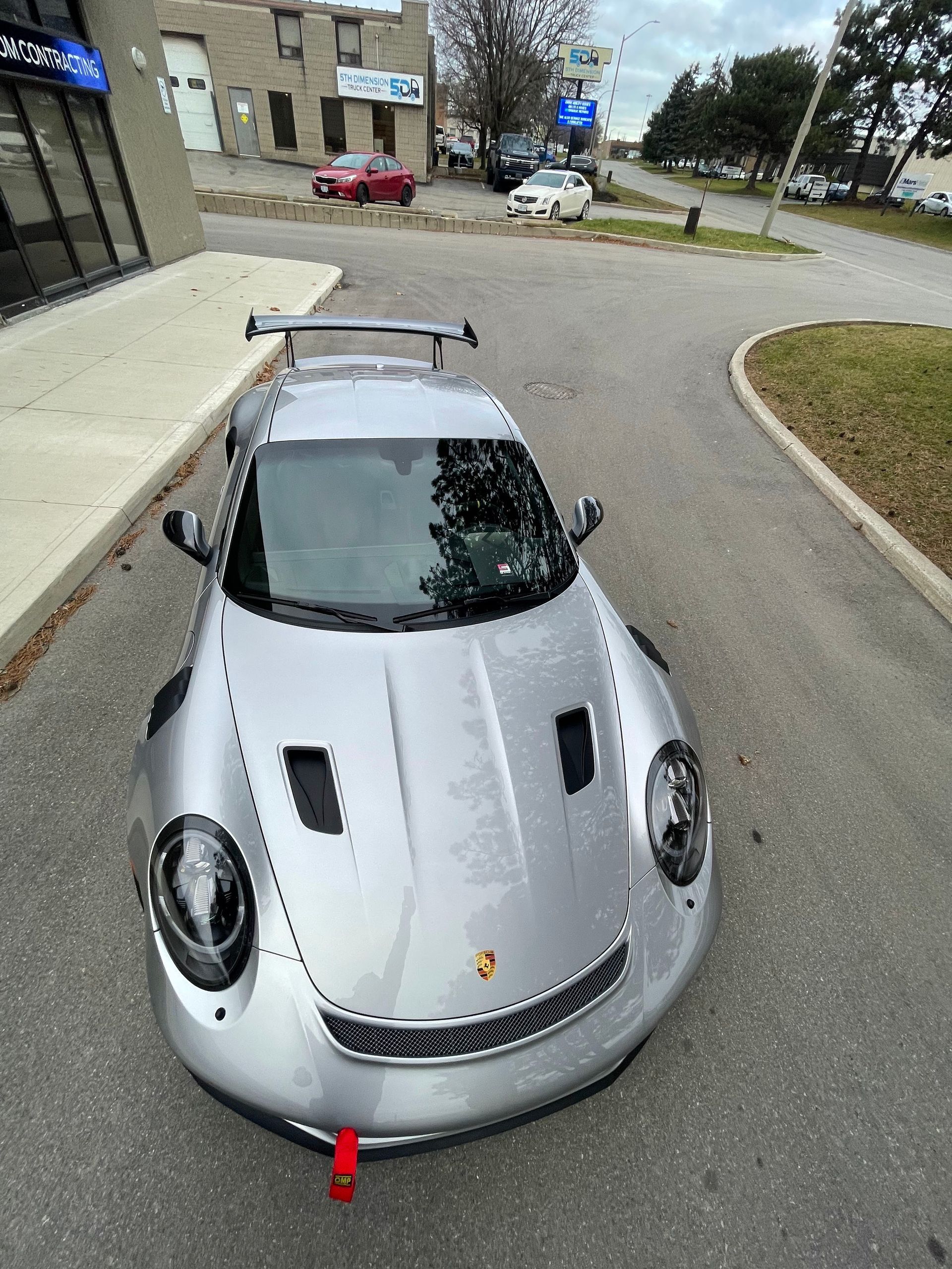A silver Porsche 911 GT3 RS with black hood vents and a large rear wing, parked in an outdoor lot.