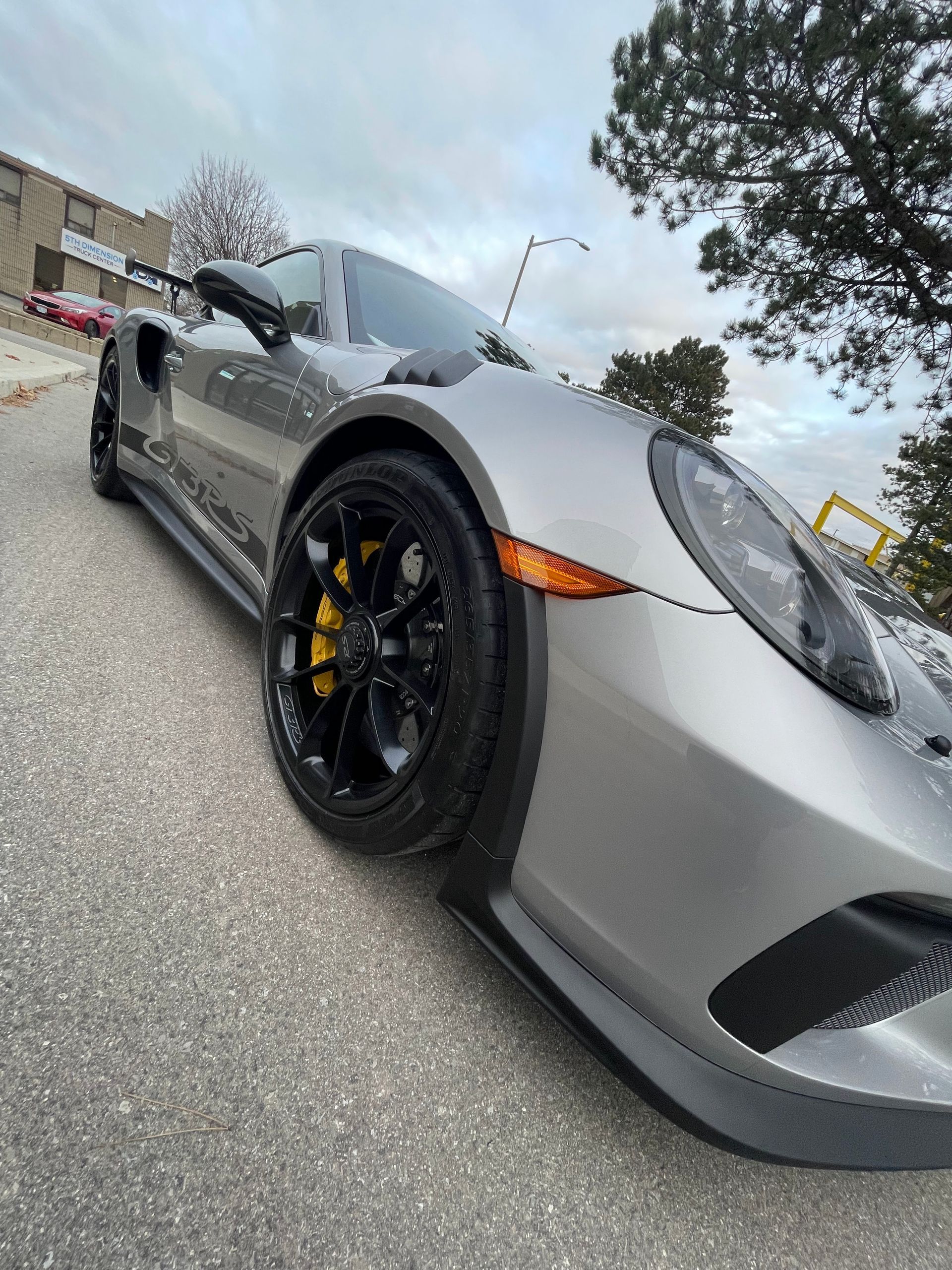 A silver Porsche 911 GT3 with black wheels and yellow brake calipers parked on an asphalt lot.