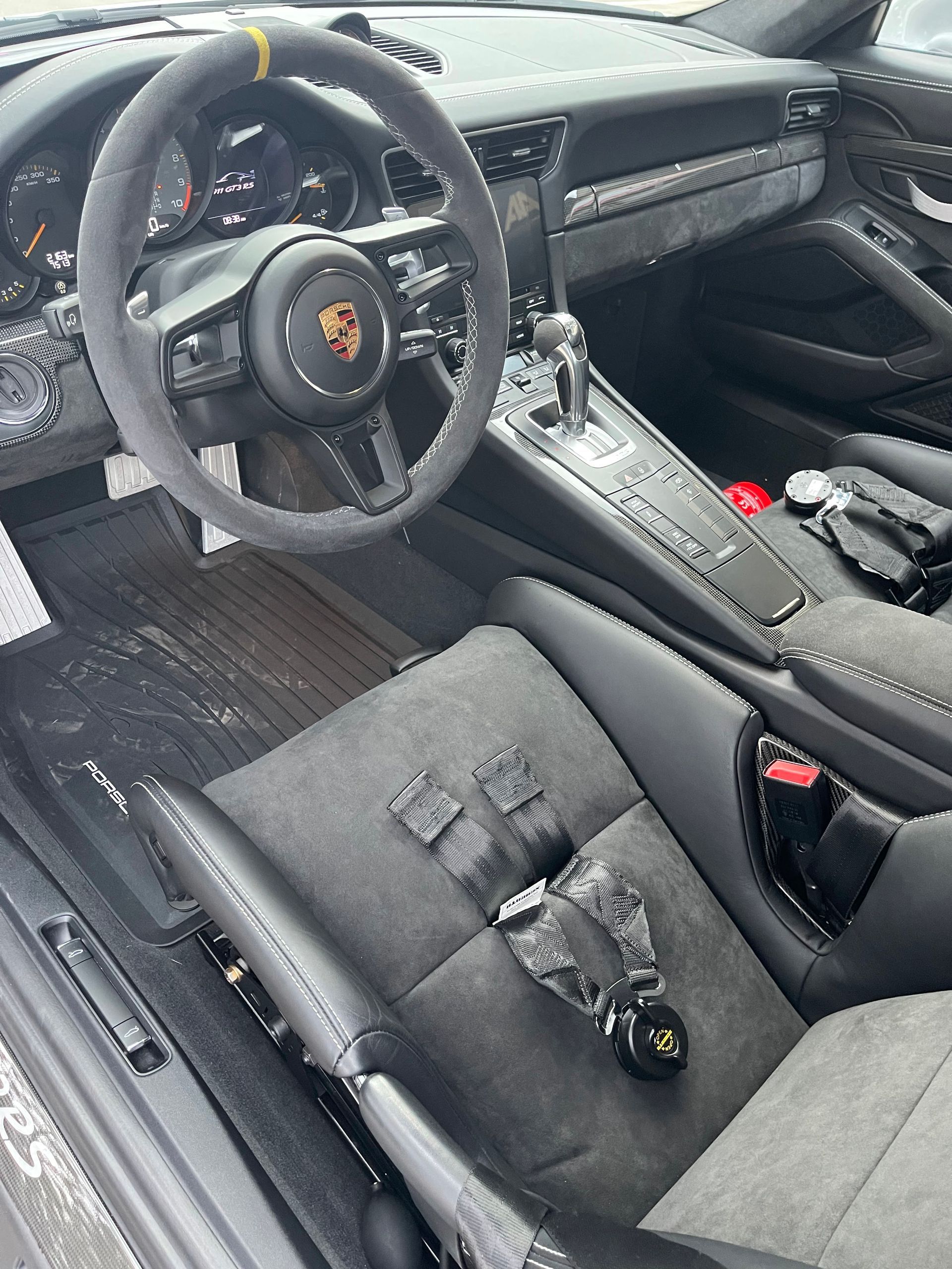 Interior of a Porsche sports car featuring a grey Alcantara steering wheel with yellow marker, bucket seats, and trim.