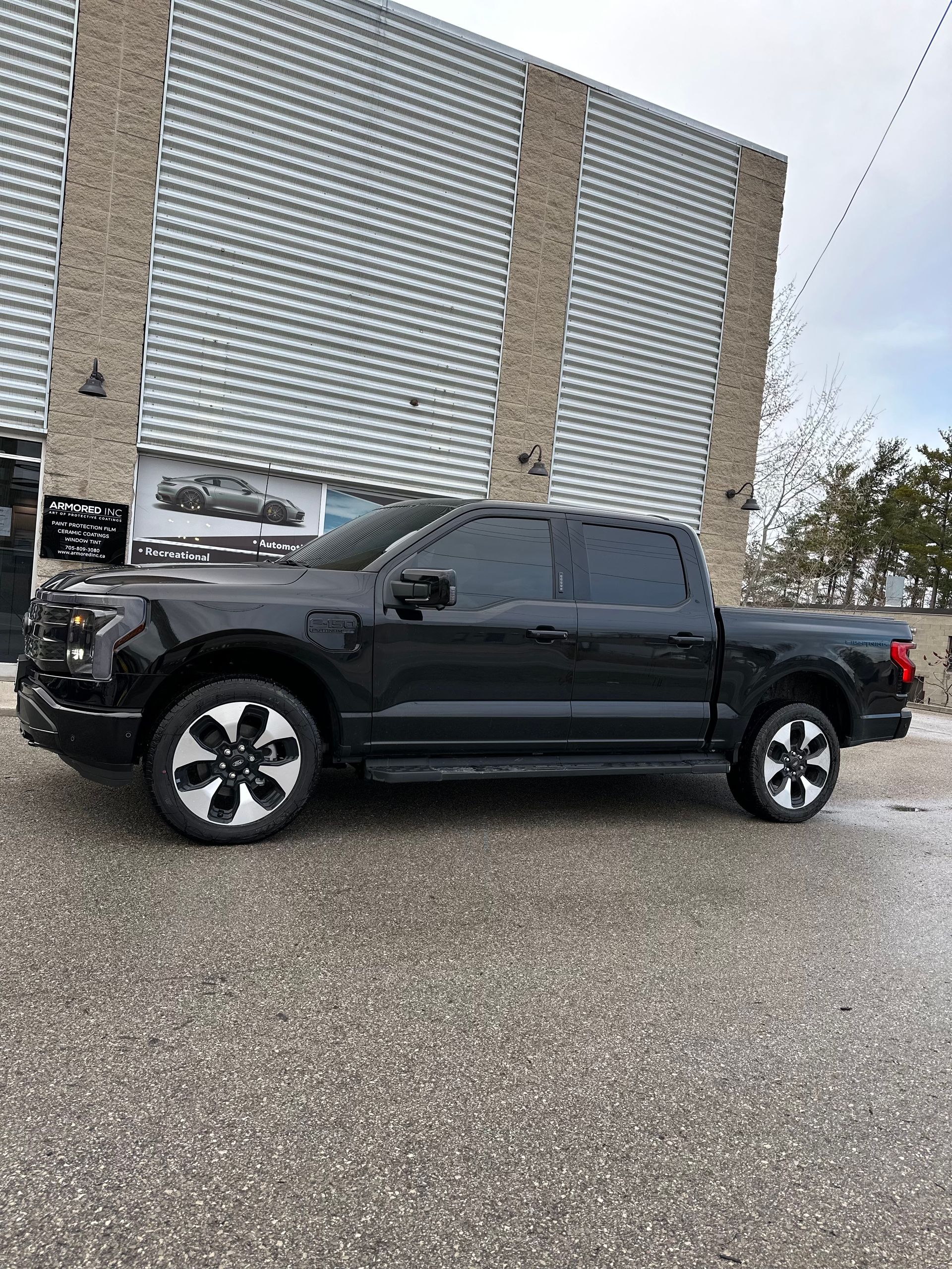 A black Ford F-150 Lightning pickup truck parked outside a building with light-colored corrugated metal siding.