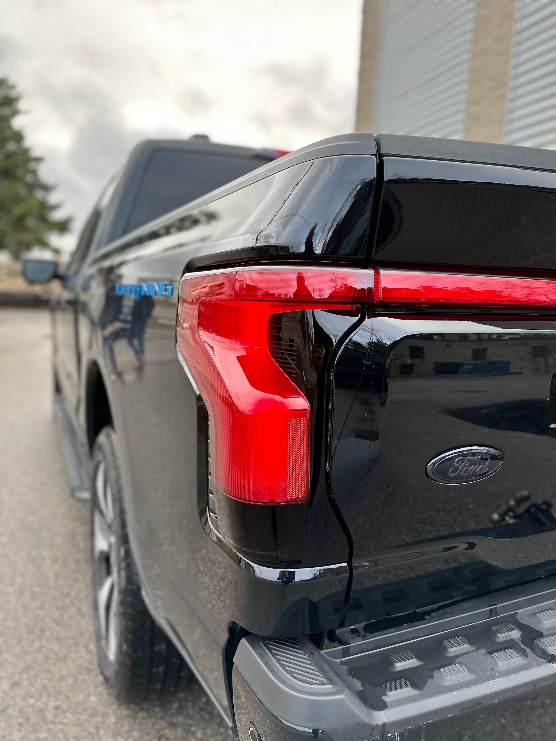 Close-up, low-angle view of the driver's side taillight and rear corner of a black Ford F-150 Lightning pickup truck.