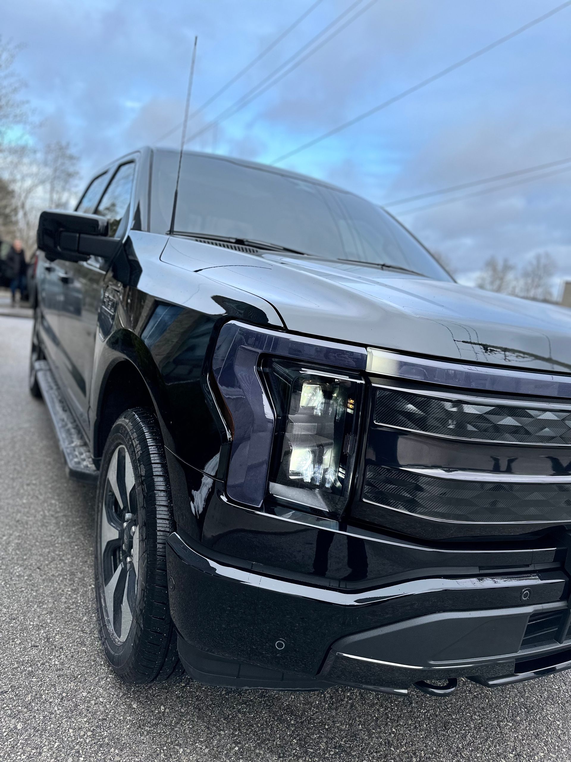 Low-angle view of a shiny black Ford F-150 Lightning electric pickup truck parked on an asphalt lot.