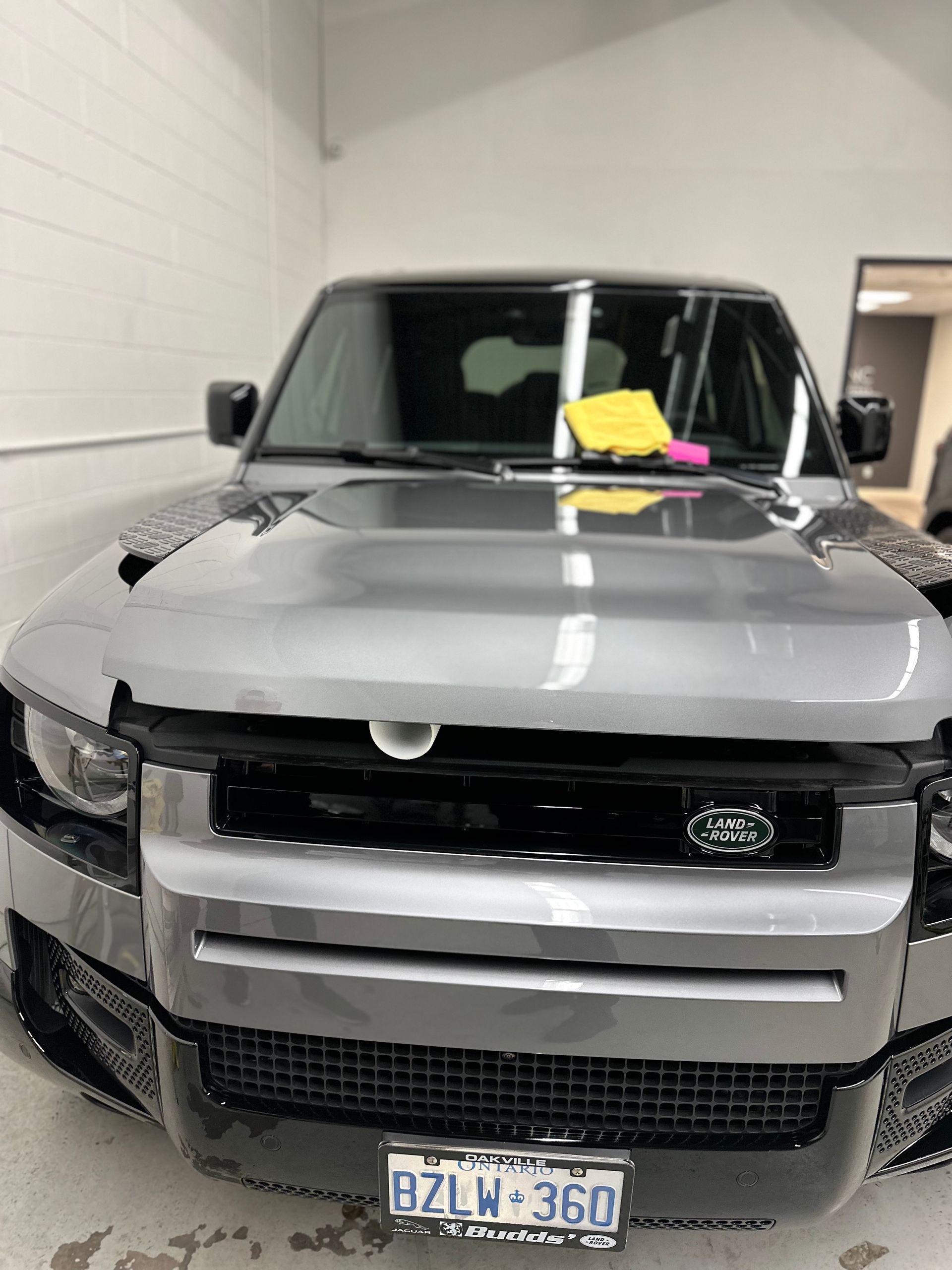 A silver Land Rover Defender parked indoors with a yellow cloth on the dashboard and an Ontario license plate.