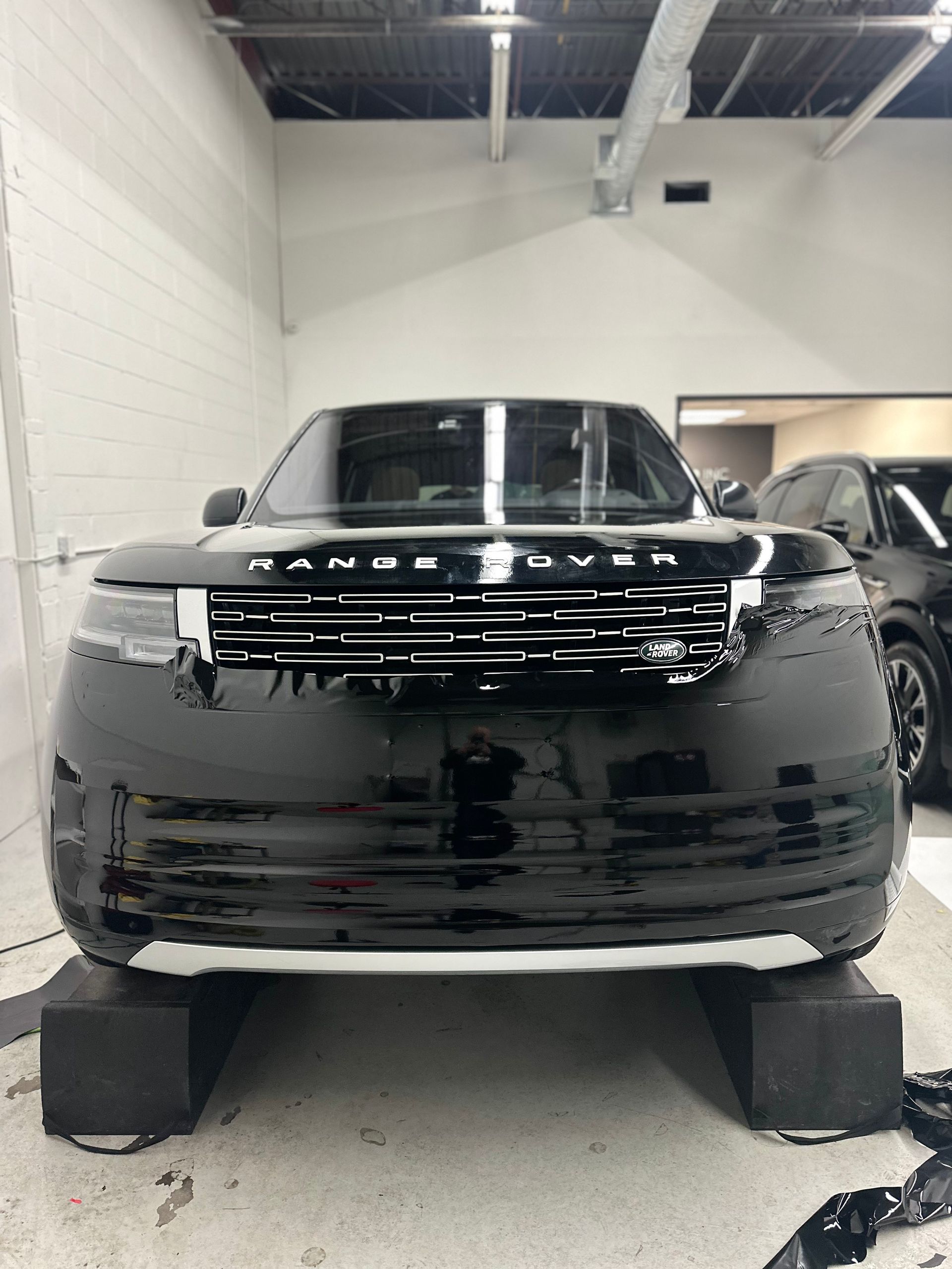 A black Range Rover parked in a garage, with the front wheels raised on black ramps for service.