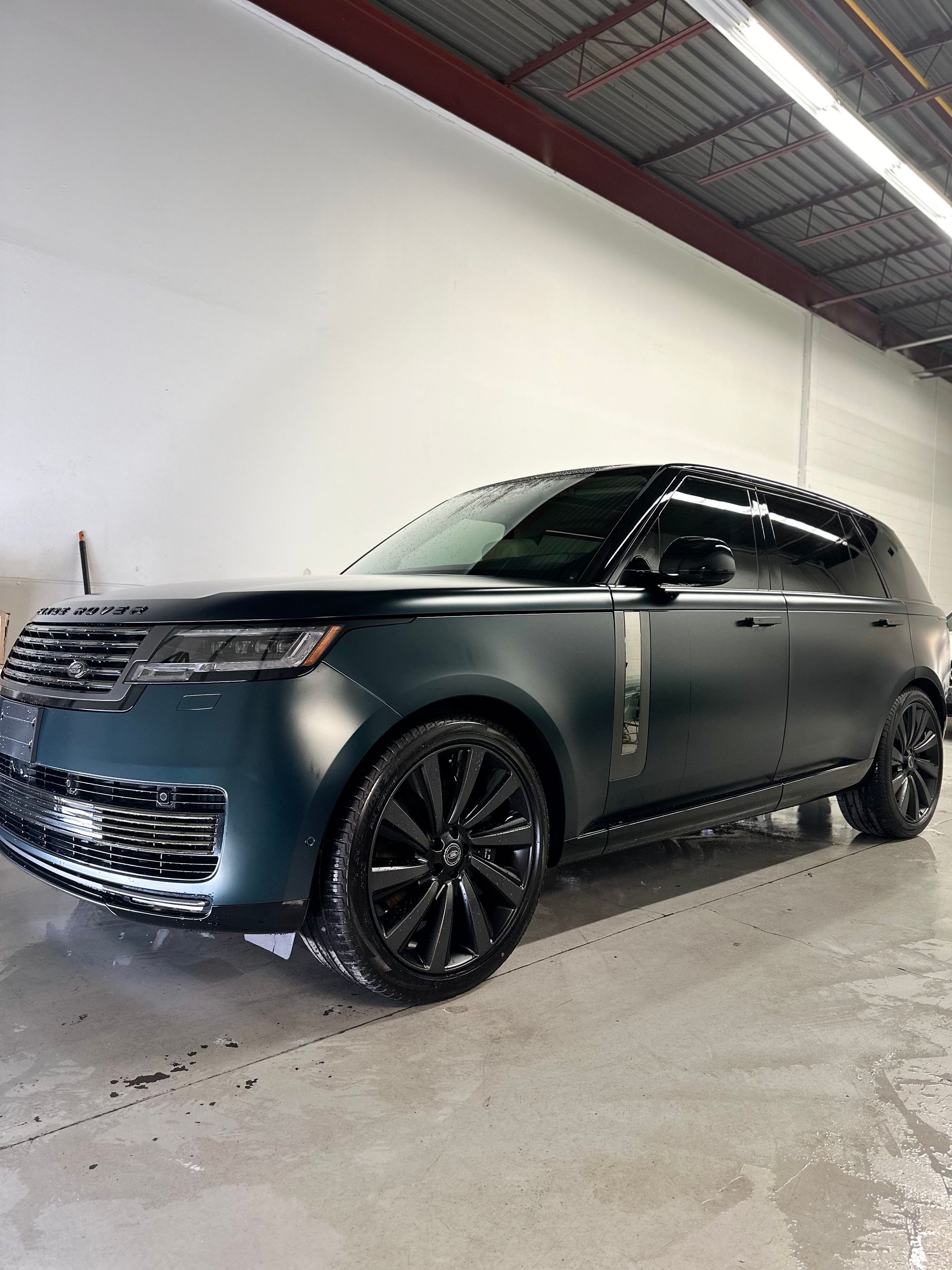 A matte black Range Rover SUV parked inside a workshop with white walls and overhead industrial lighting.