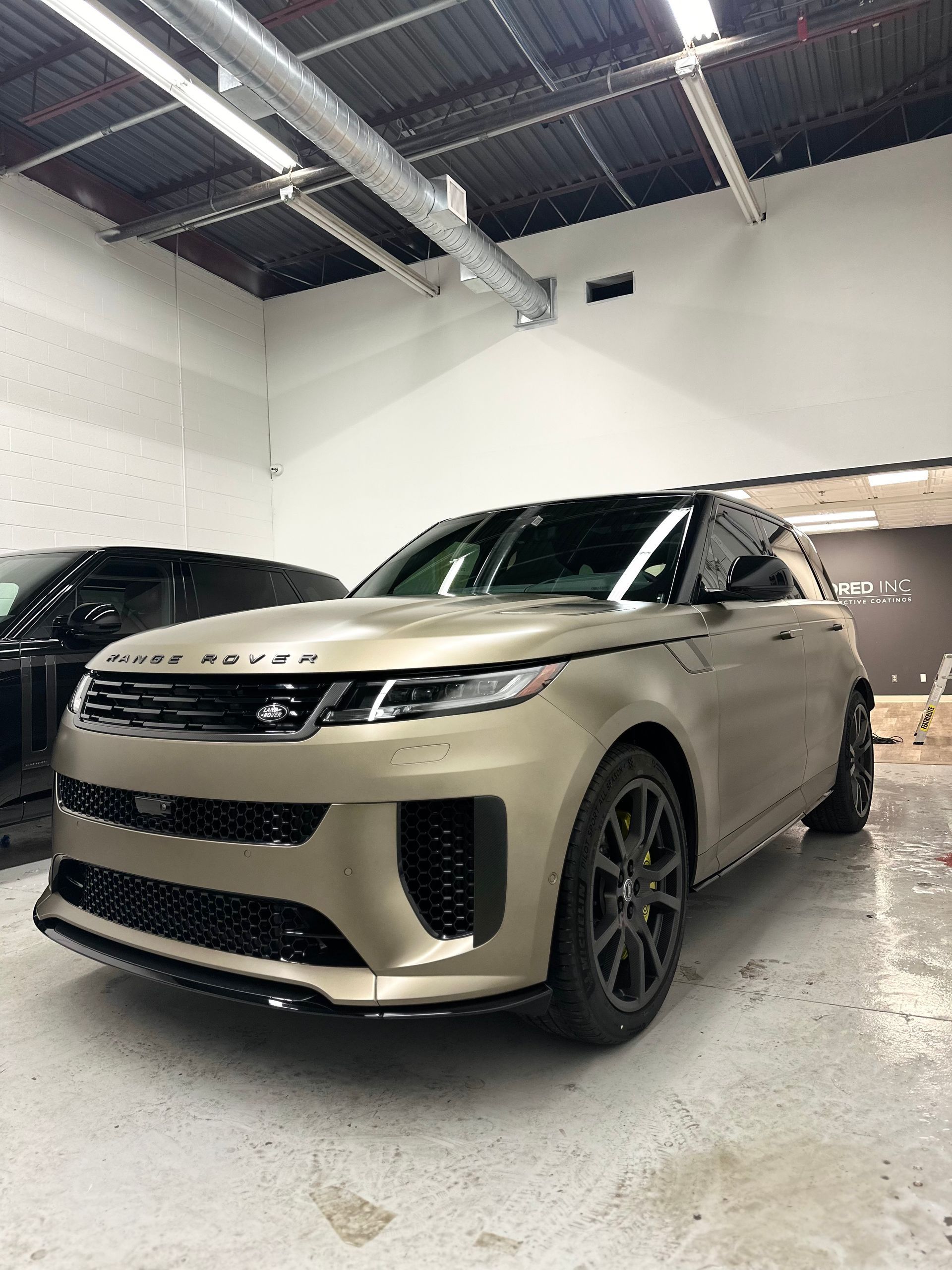 A matte gold Range Rover parked inside a brightly lit, industrial-style garage.
