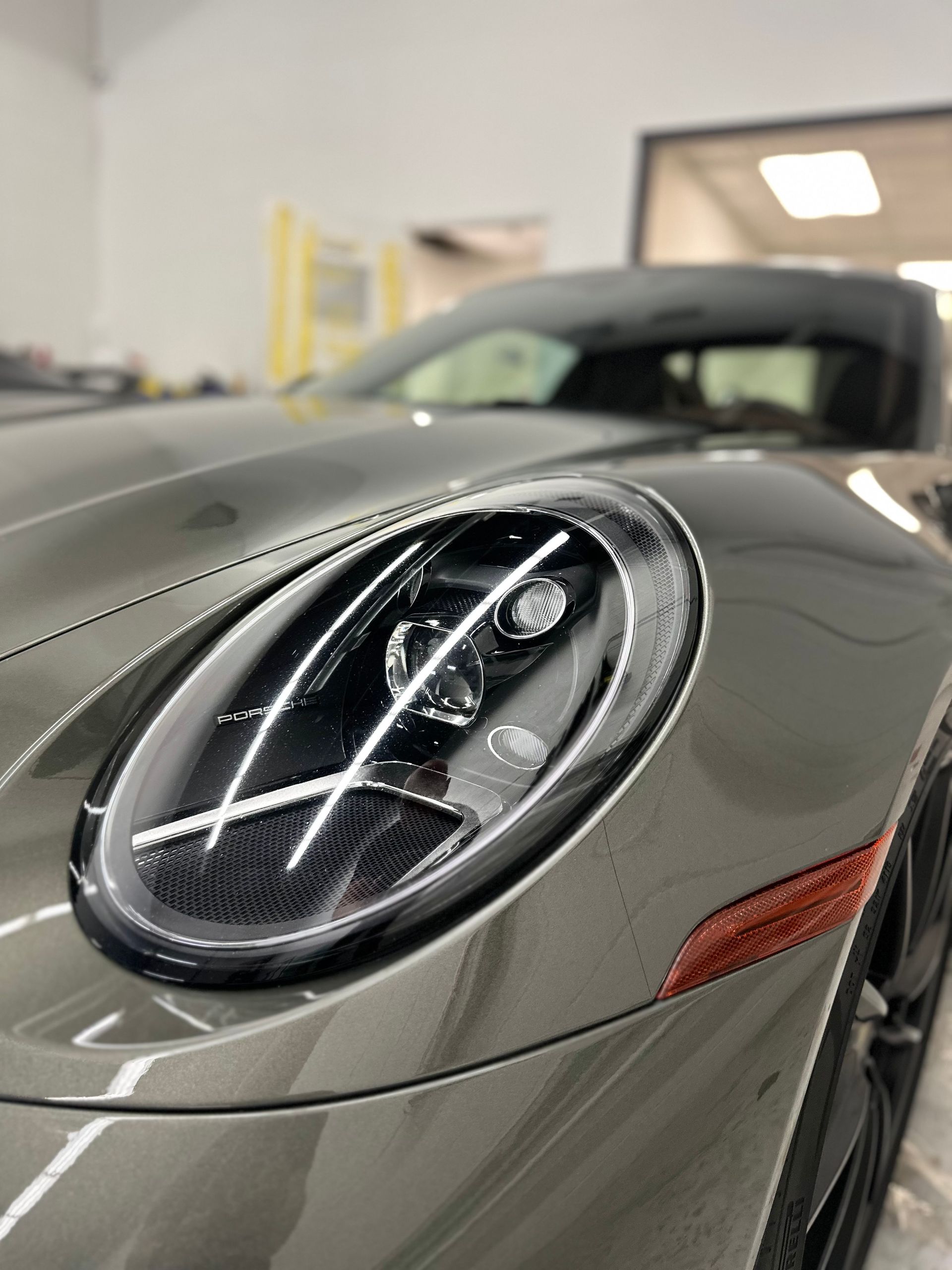 A close-up of a grey Porsche 911 headlight with distinct LED light bars, seen in a garage setting.
