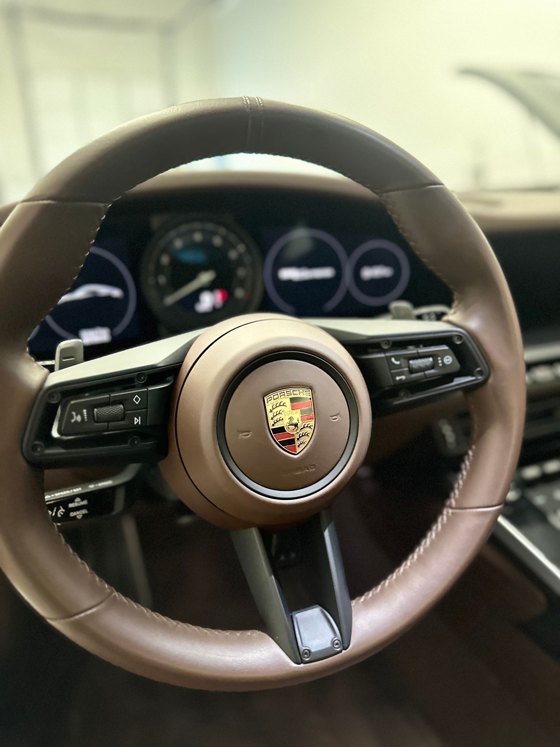 A brown leather-wrapped Porsche steering wheel with a centered crest and digital dashboard in the background.