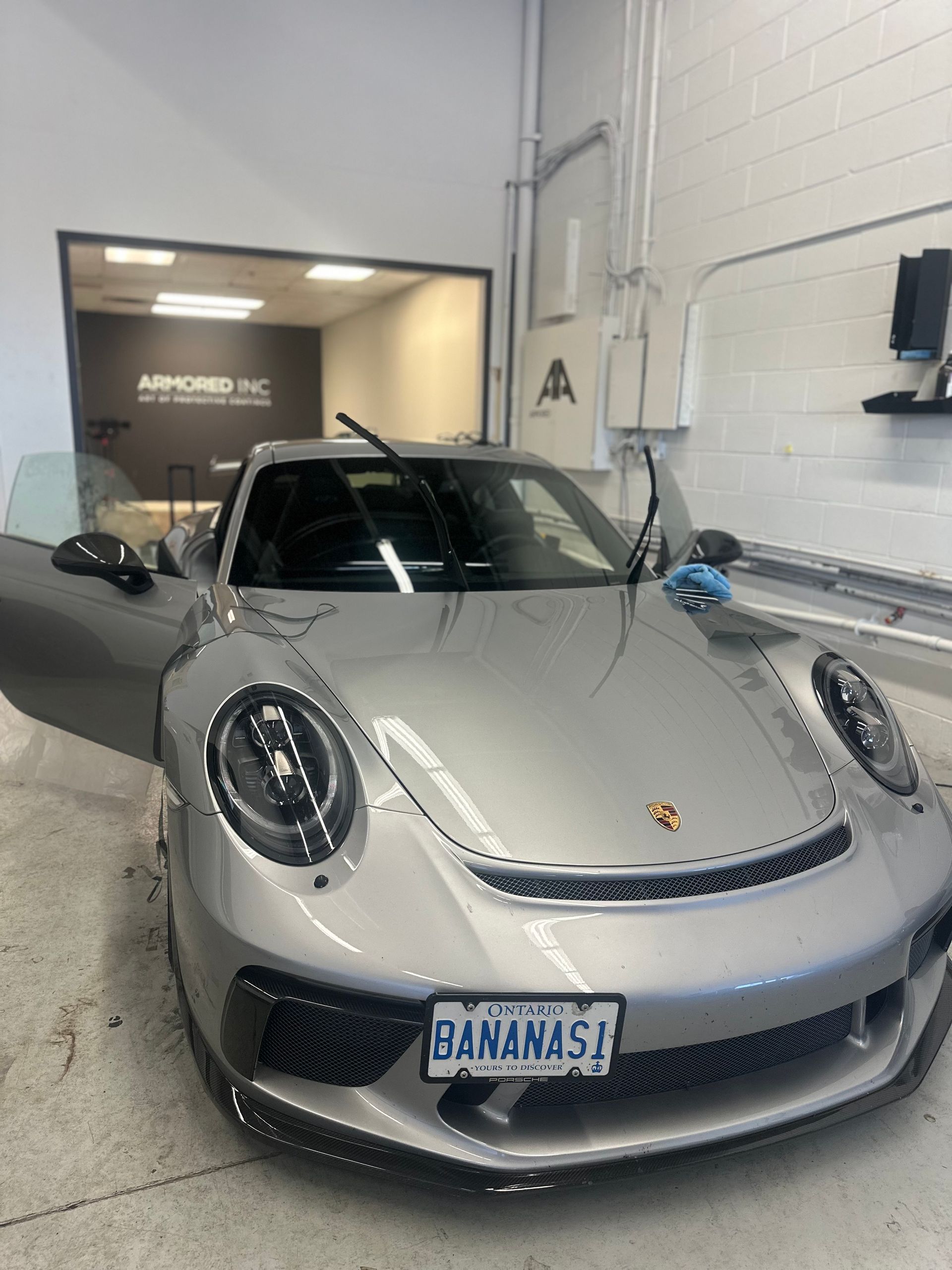 A silver Porsche 911 parked inside a garage with its hood open and 