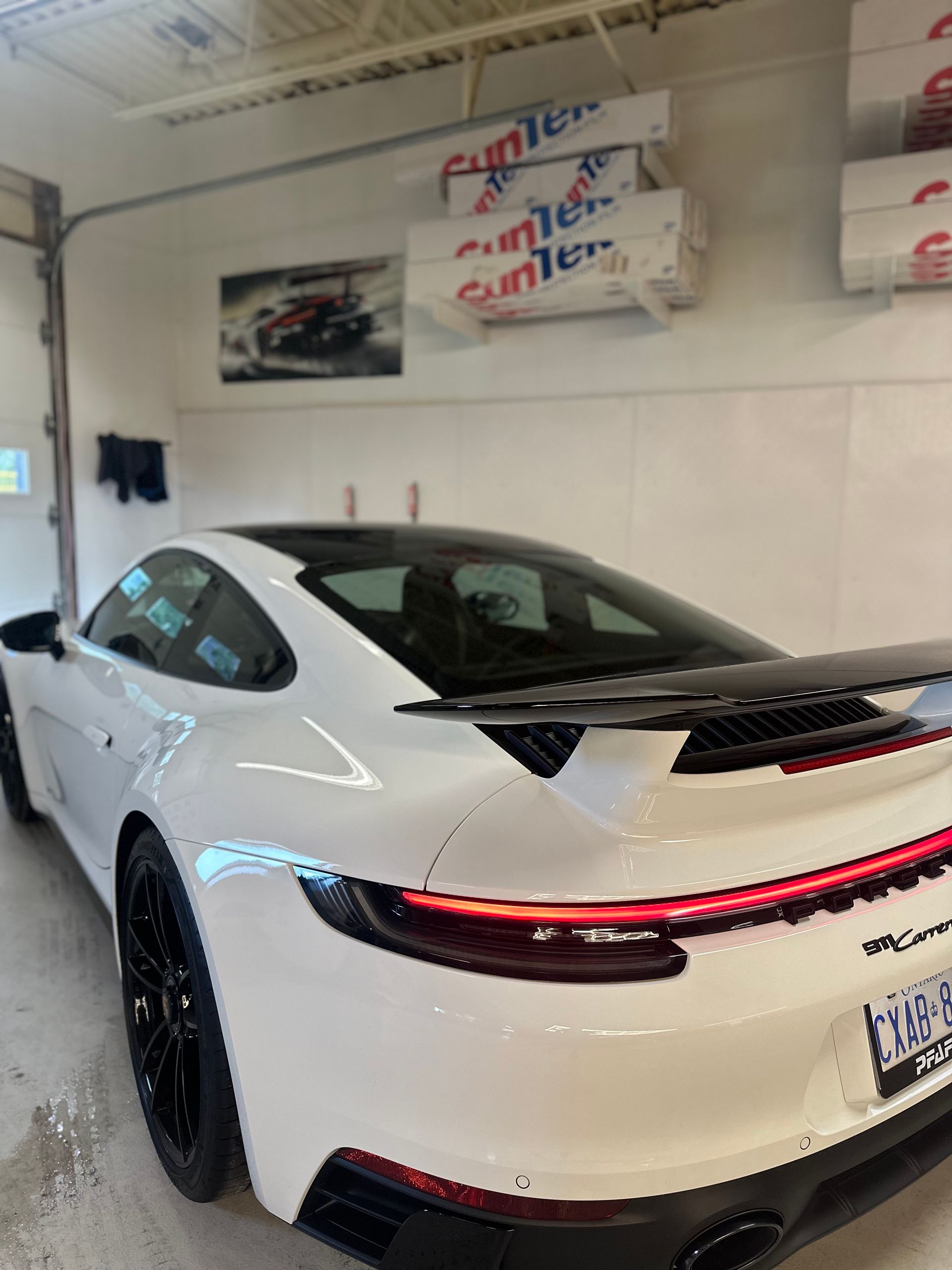 A white Porsche 911 Carrera with a black rear wing and black wheels parked inside a garage.