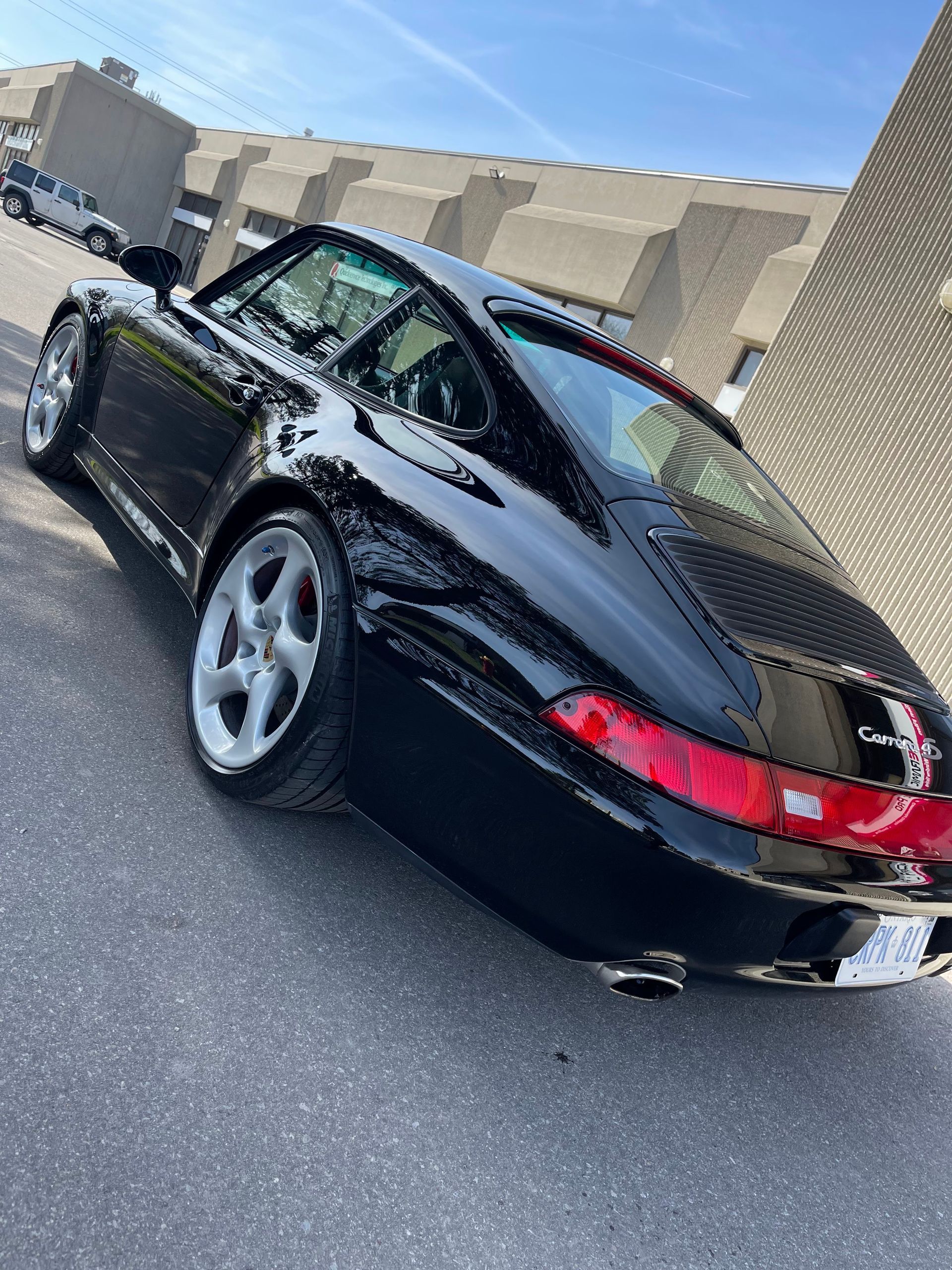 A black Porsche 911 Carrera parked on asphalt near a large building.