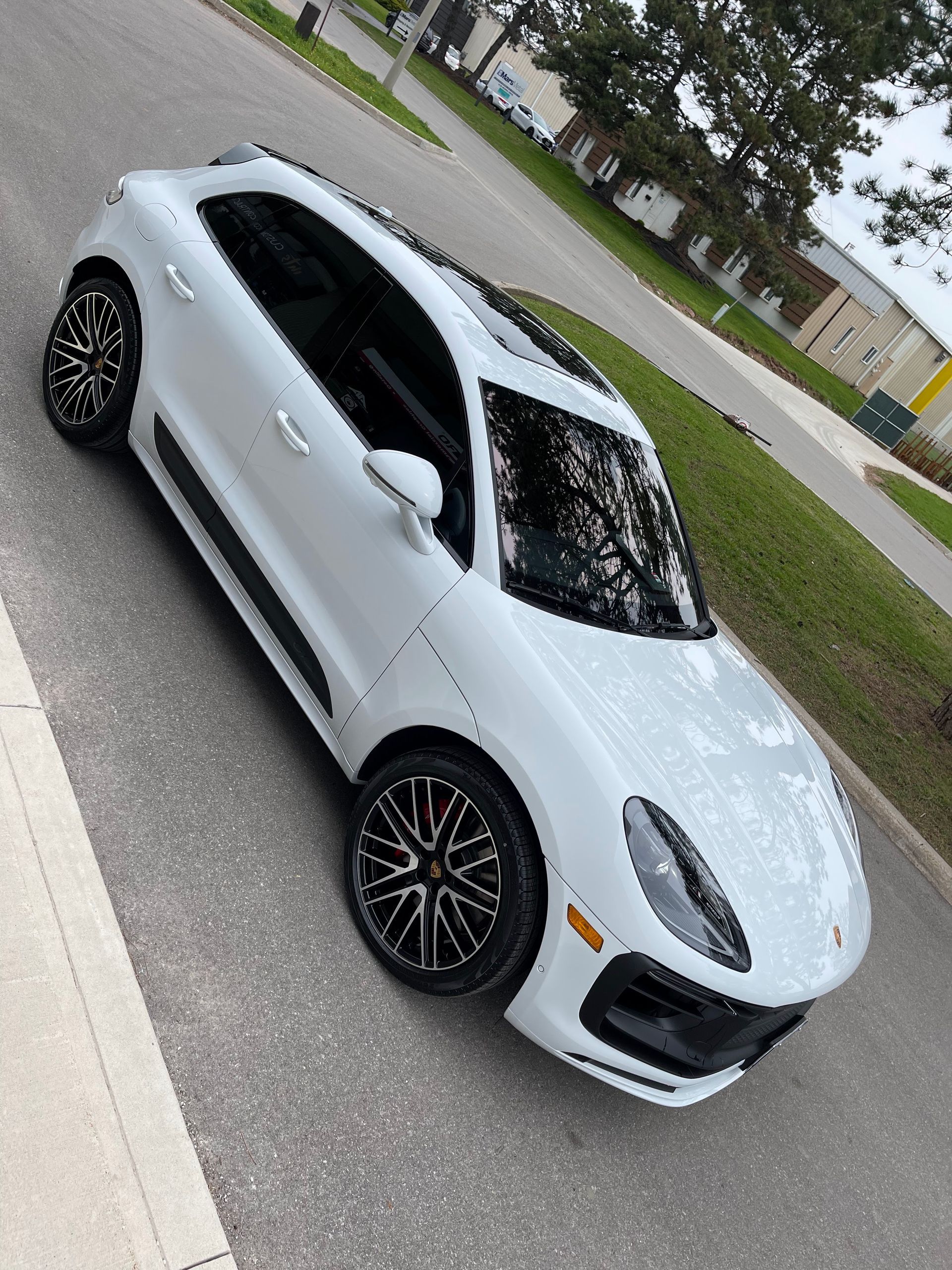 A white Porsche Cayenne SUV with black rims parked on an asphalt street next to a grassy curb.