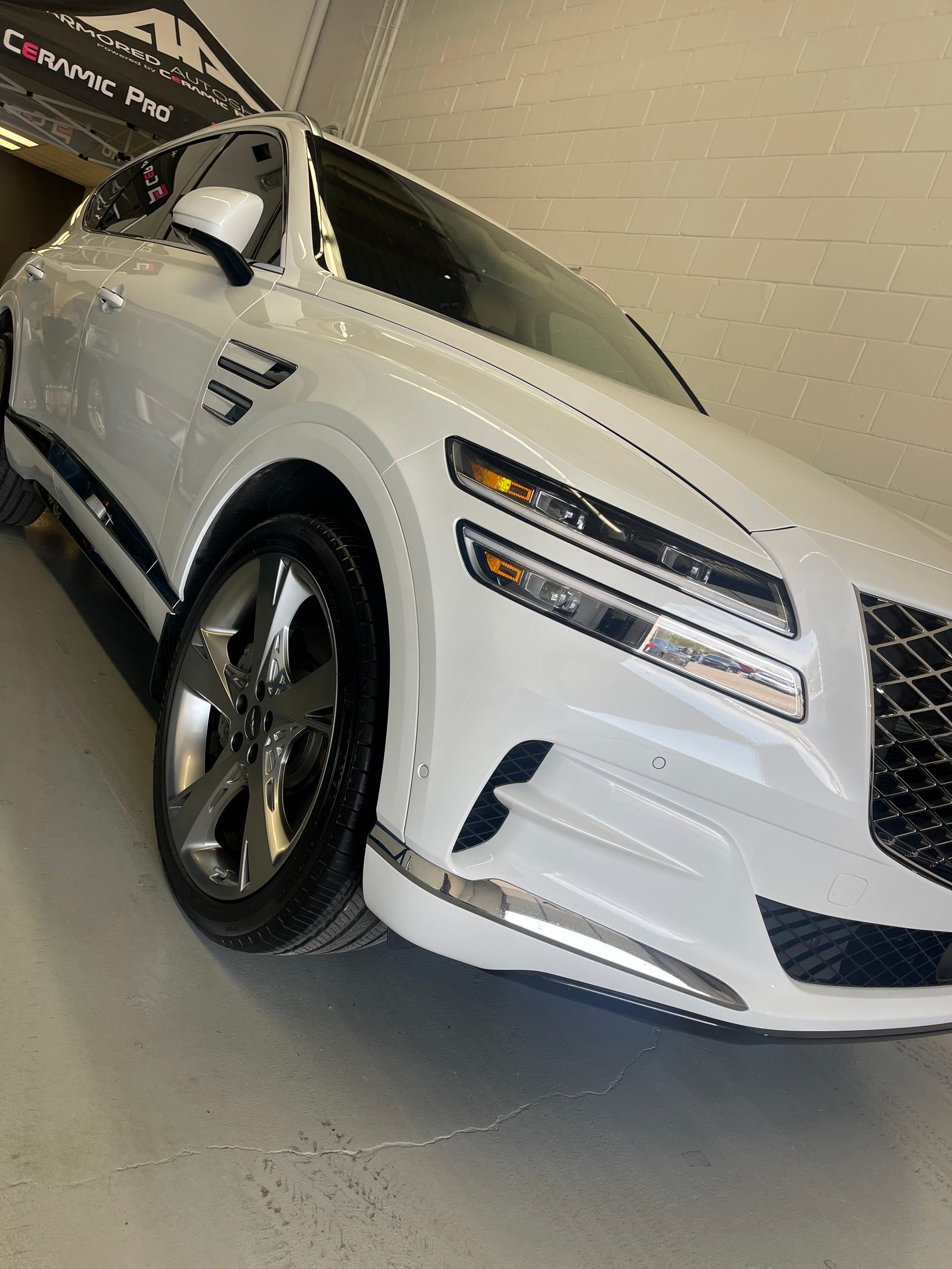 A white Genesis GV80 SUV parked inside a garage, captured from a low angle.