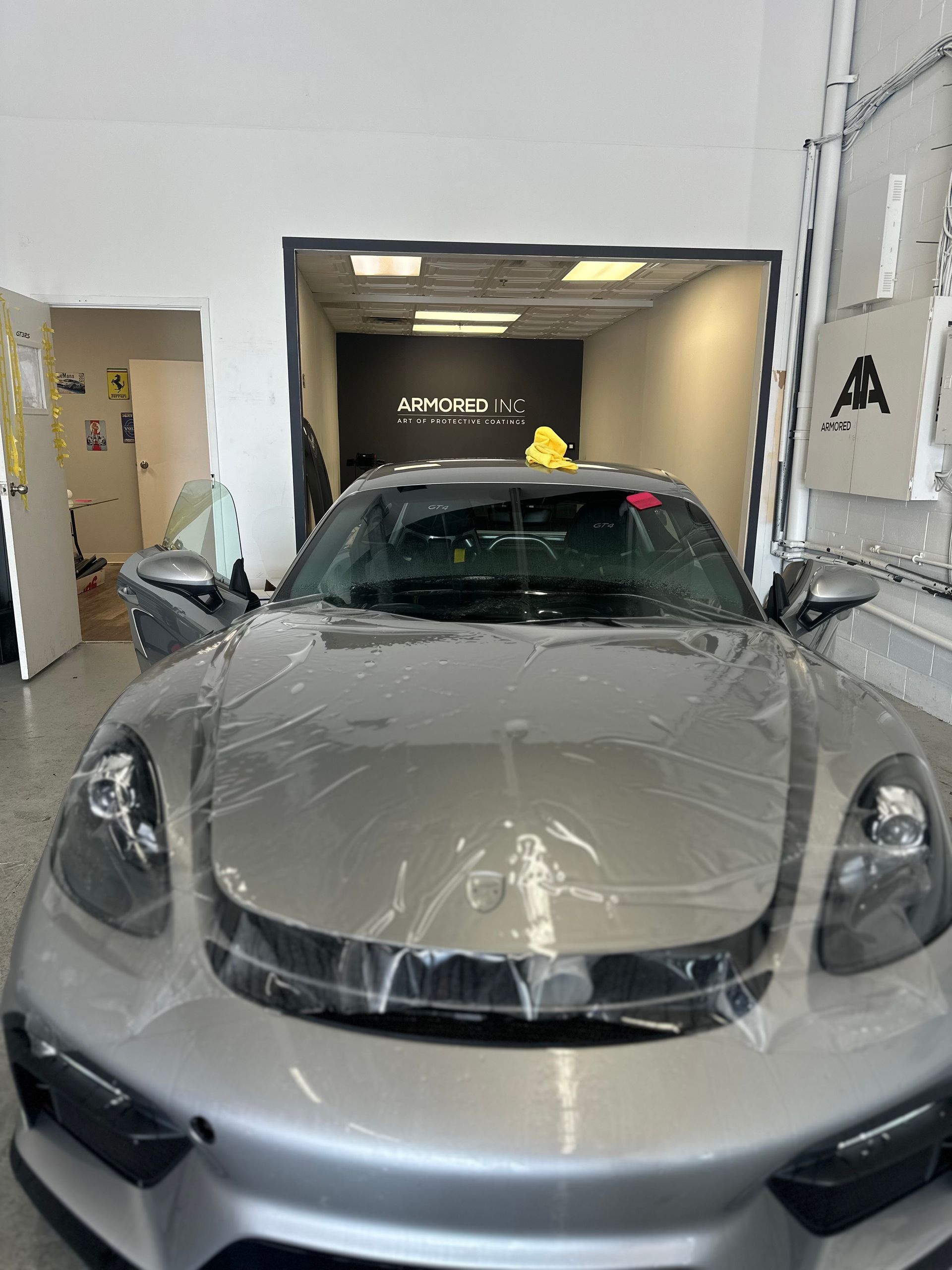 A silver Porsche inside a shop with protective film partially applied to its hood.
