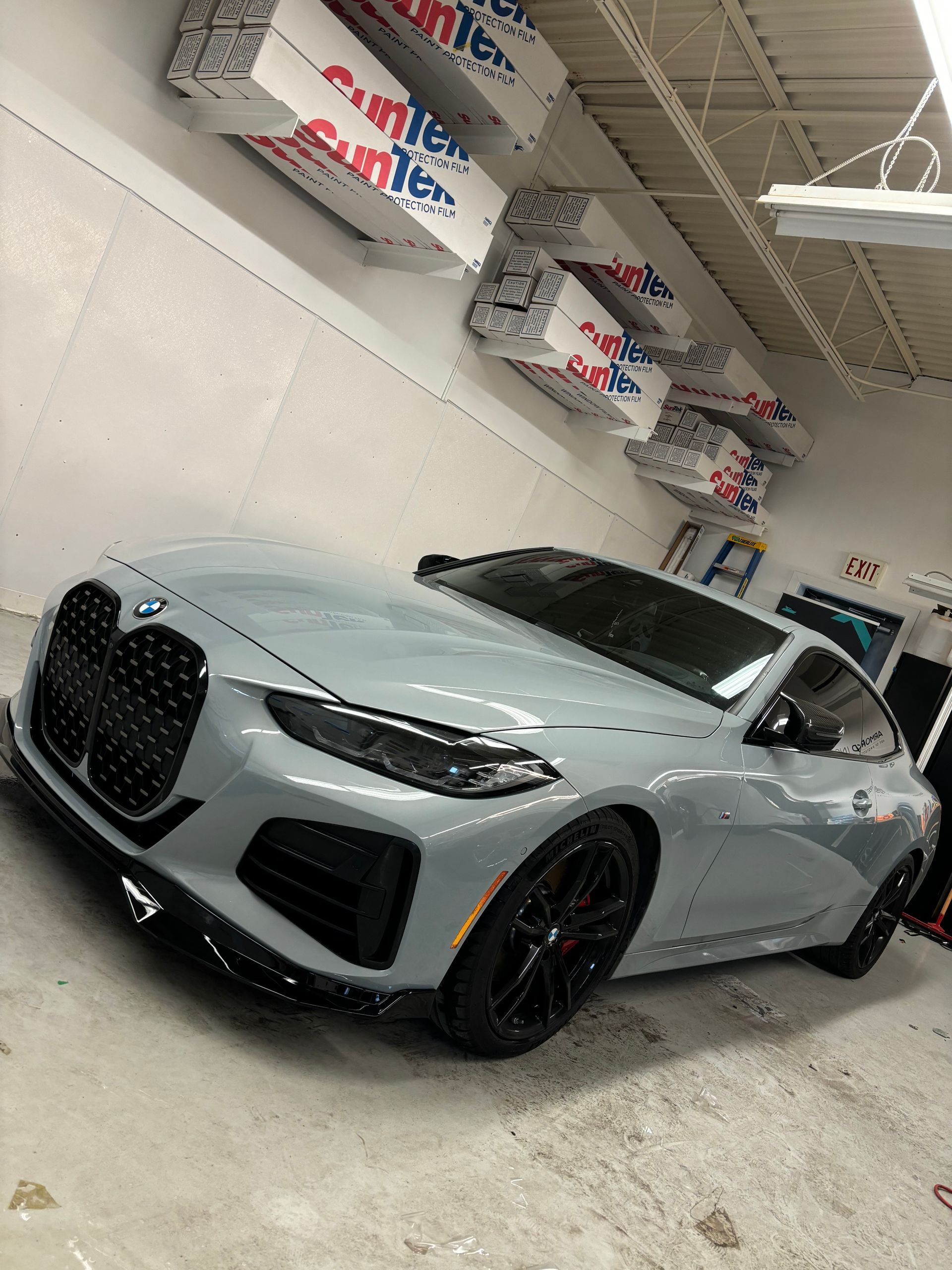 A gray BMW coupe with a black grille and black wheels parked in a garage with insulation rolls on the ceiling.