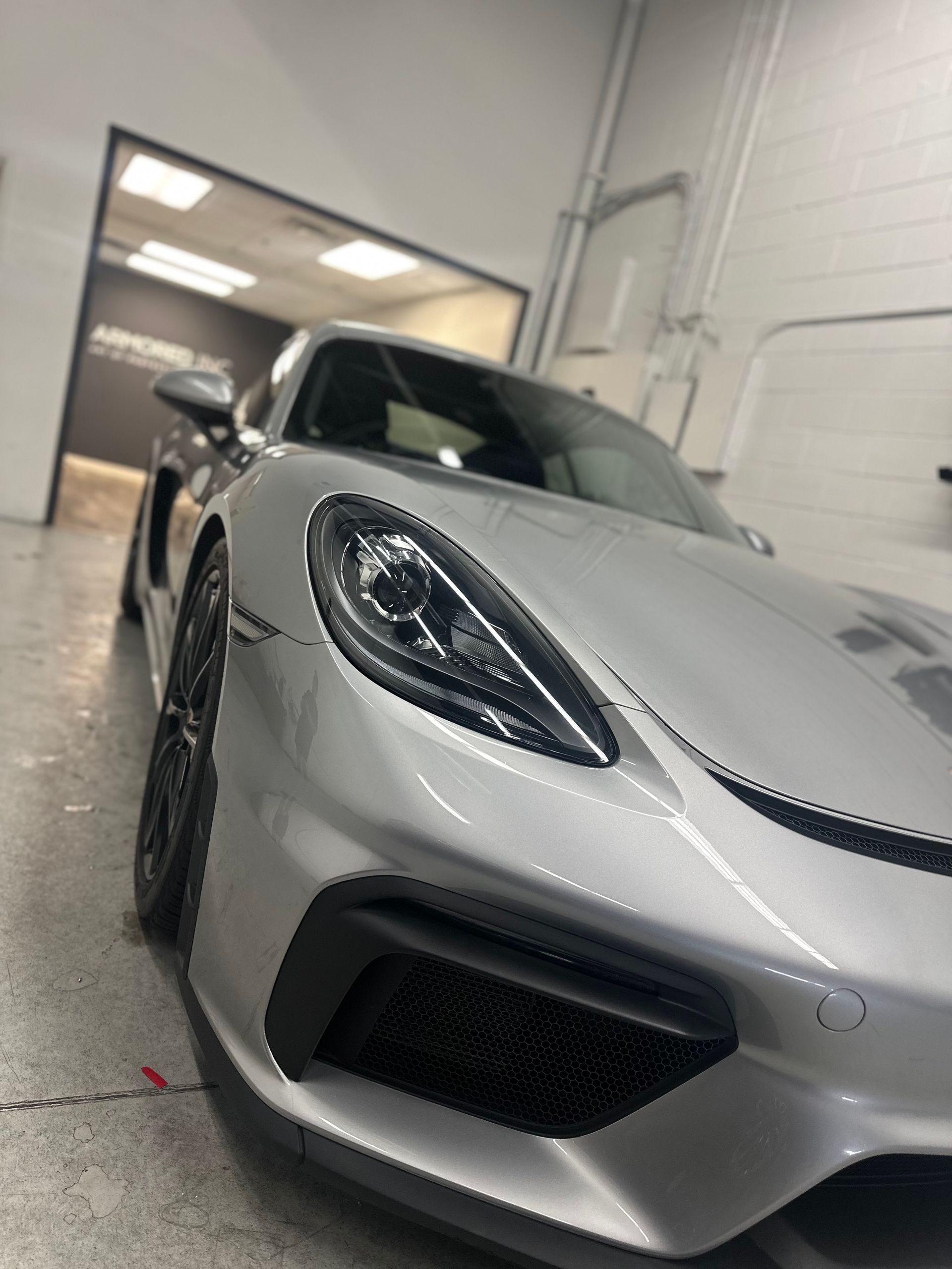 A low-angle view of a silver Porsche parked in a brightly lit professional garage or auto shop.