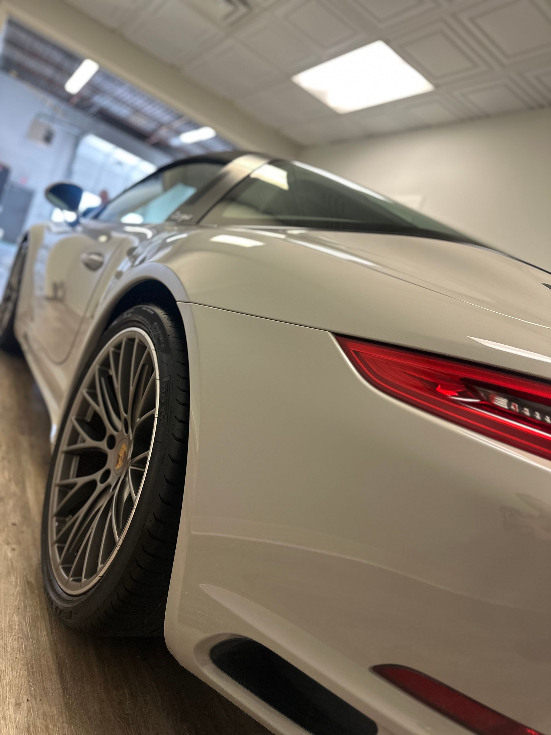 A white Porsche 911 Targa, angled to show its rear wheel, taillight, and signature roll hoop, parked inside a garage.