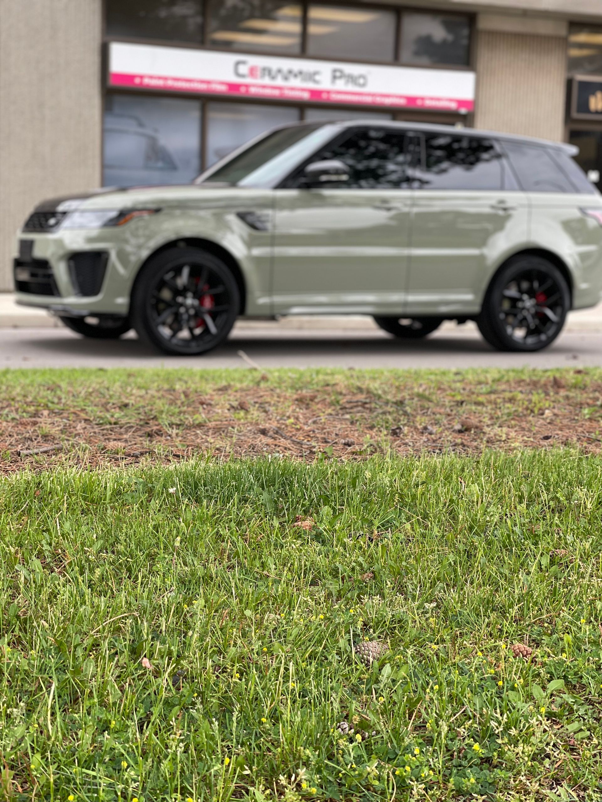 A light green Land Rover Range Rover parked in front of a Ceramic Pro shop with a green lawn in the foreground.