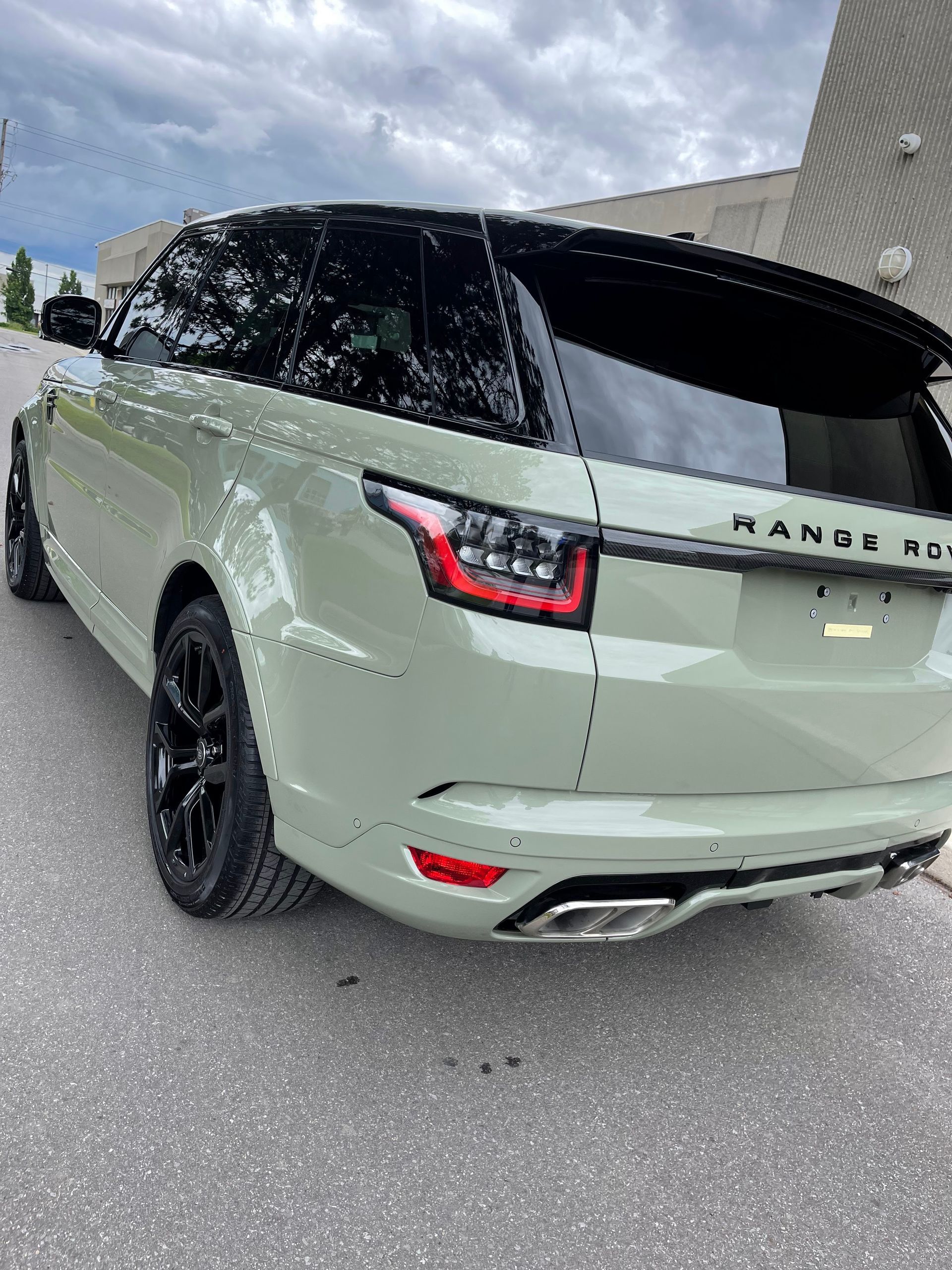 Sage green Range Rover Sport parked outdoors with black wheels and a black roof.