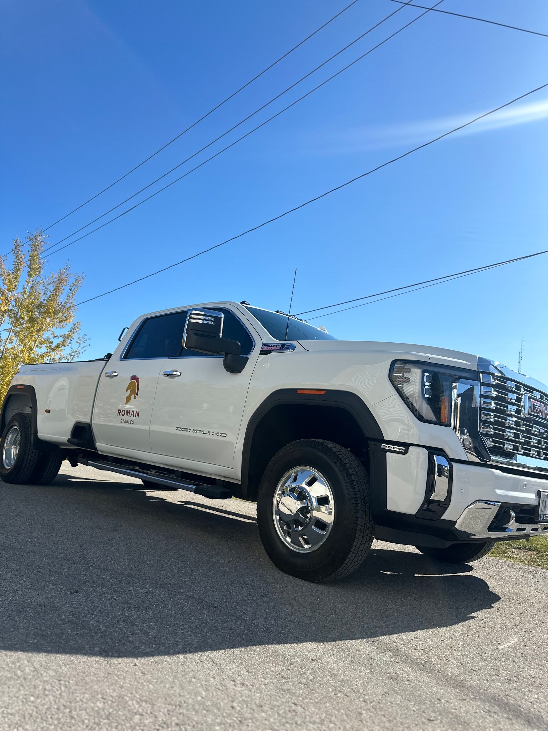 A white GMC dually pickup truck parked on a gravel lot under a clear blue sky.