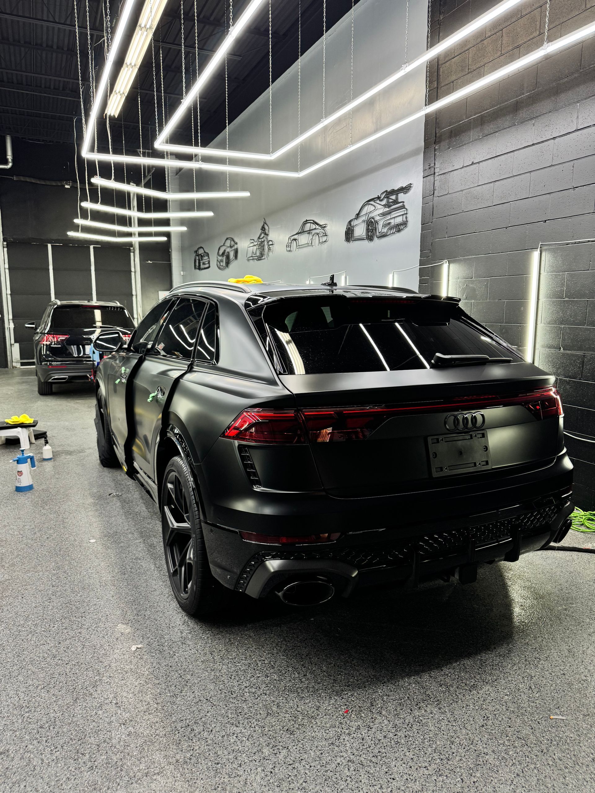 A matte black Audi RS Q8 parked inside a brightly lit professional car detailing garage.