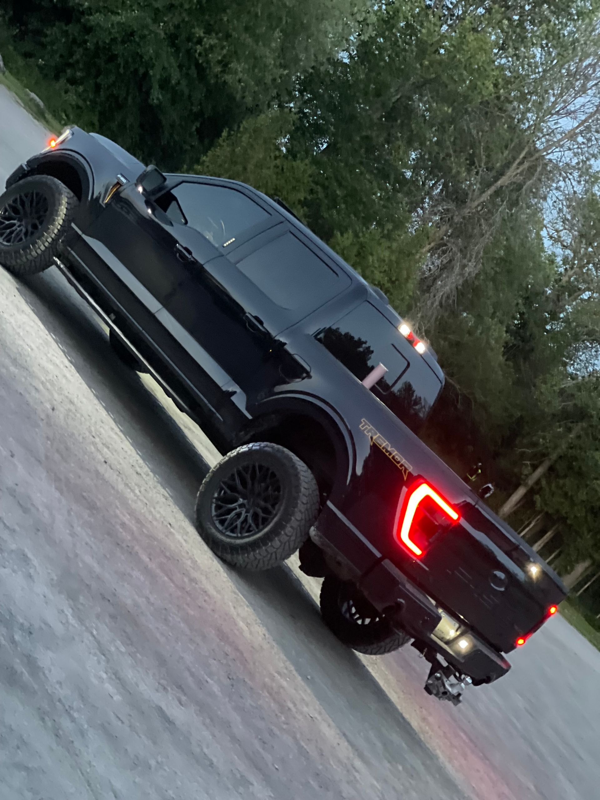 A black pickup truck parked on an asphalt surface with trees in the background during the golden hour.