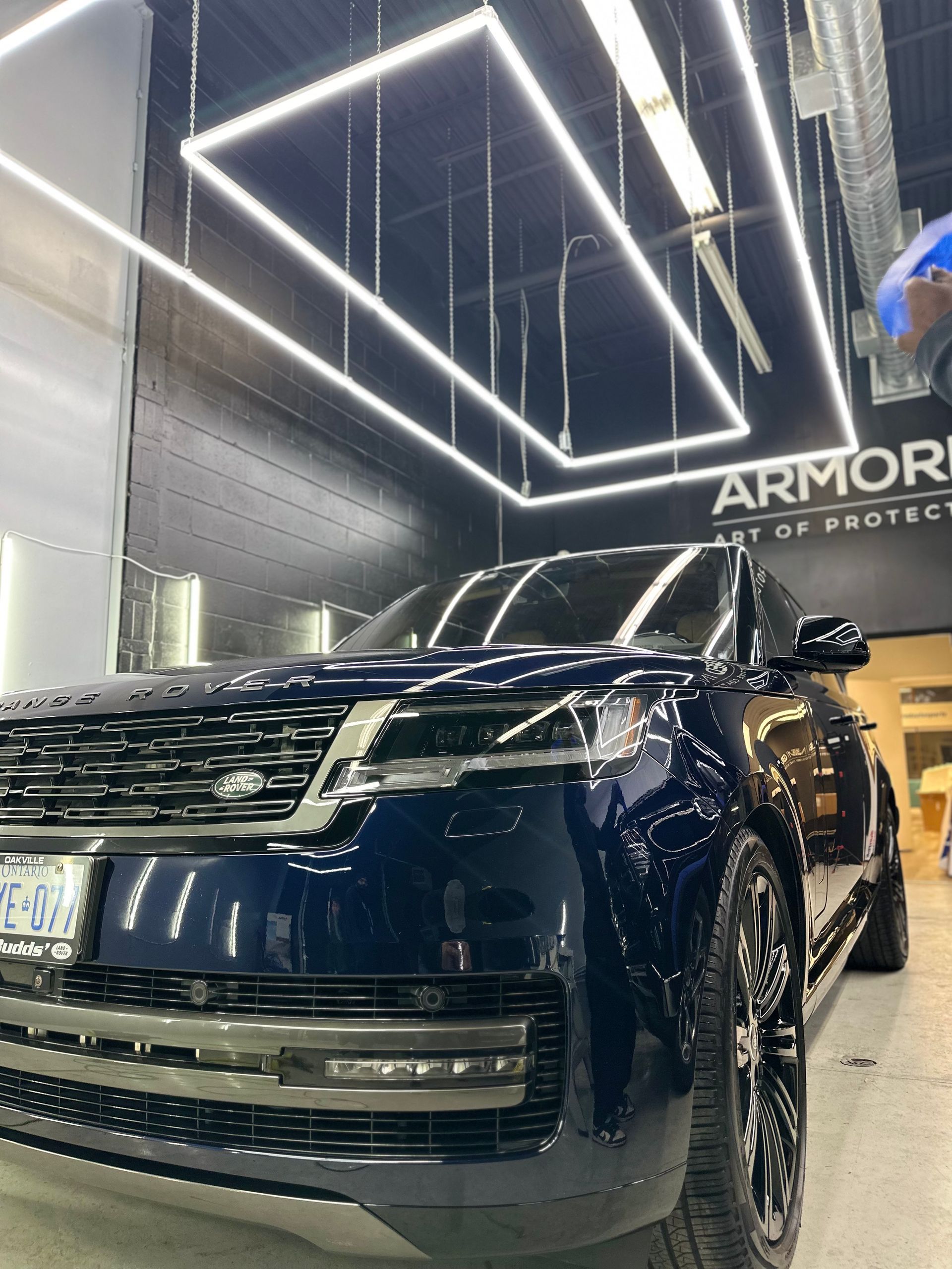 A dark blue Range Rover parked in a brightly lit professional auto detailing shop with geometric overhead lighting.