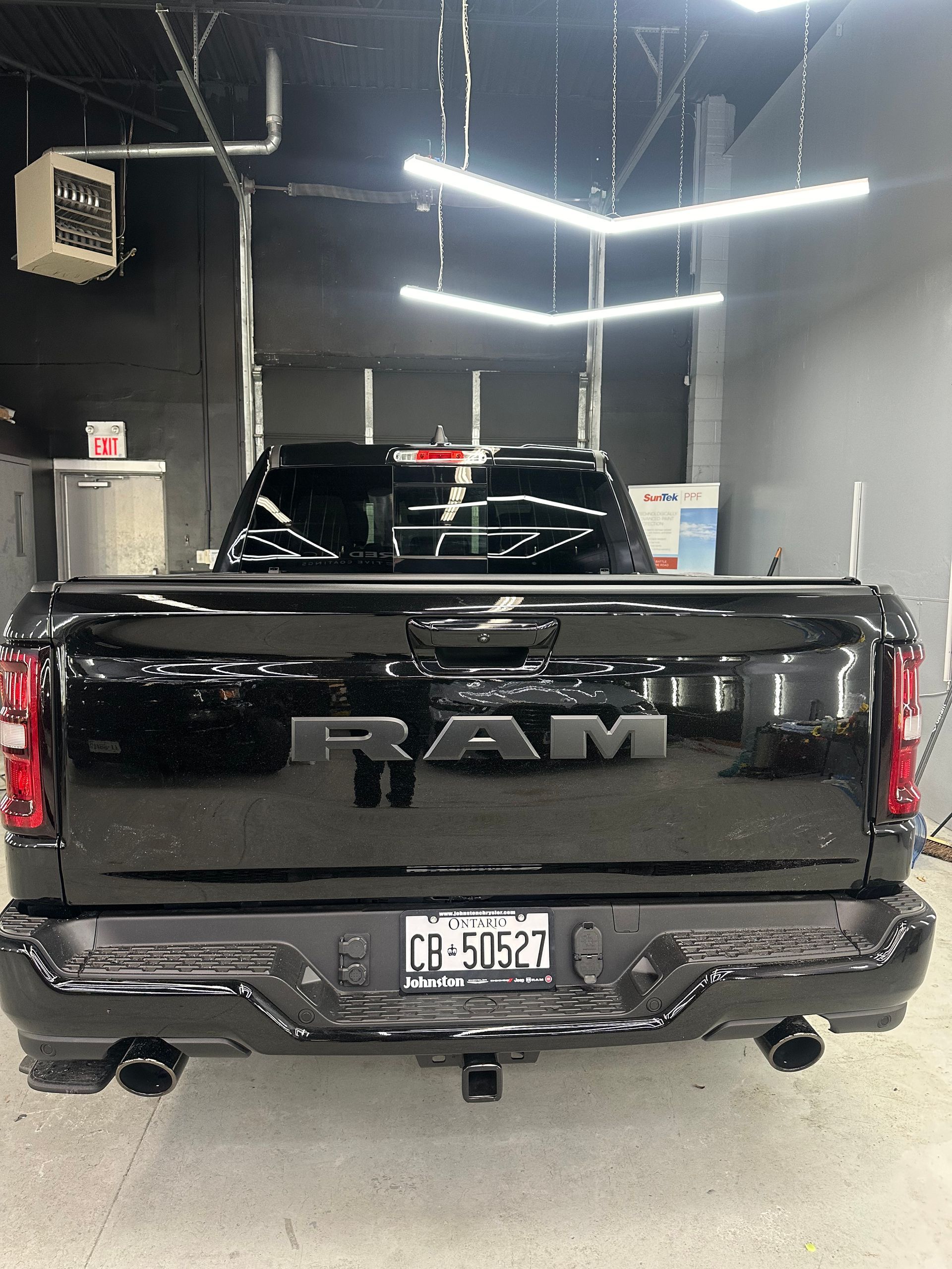 A black RAM pickup truck viewed from the rear, parked in a well-lit workshop with overhead geometric lighting.