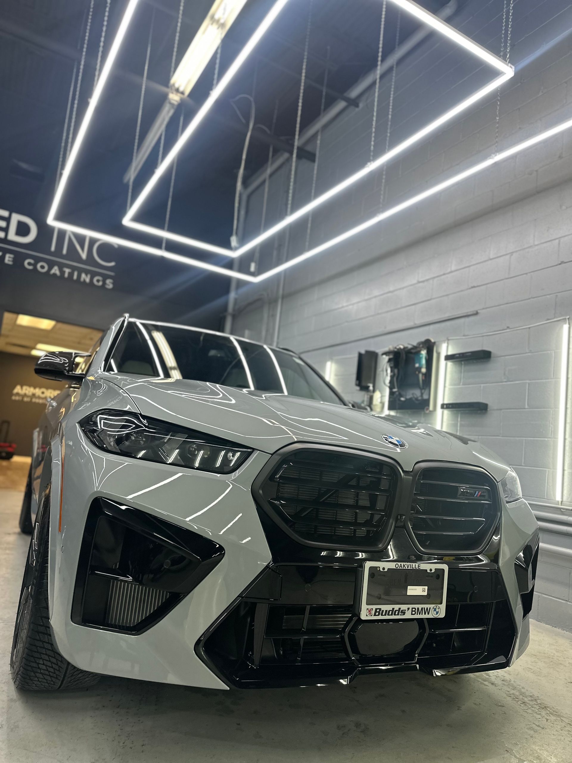 A gray BMW SUV with black trim and a grille is parked in a well-lit, professional automotive garage.