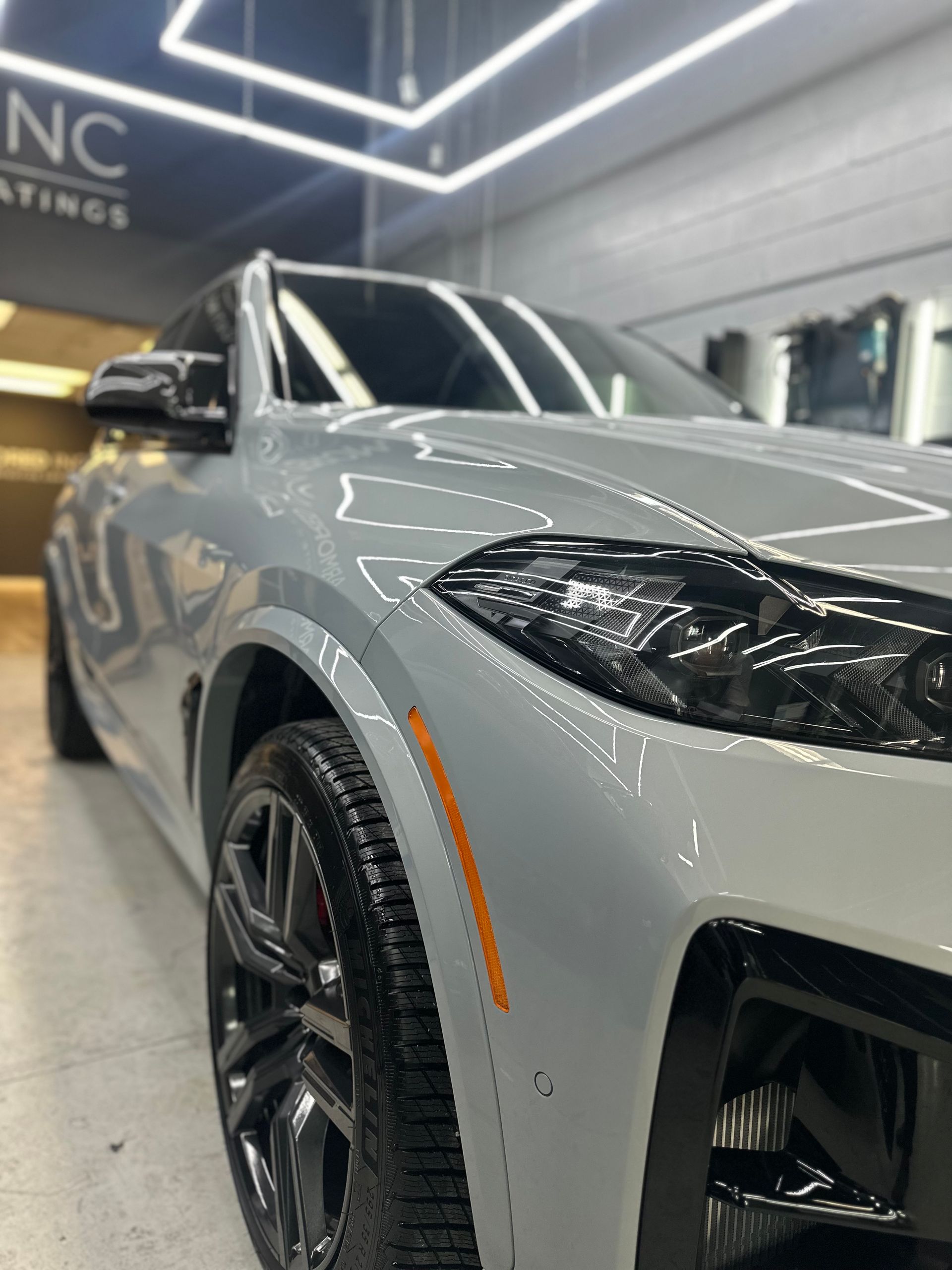 A glossy, light-gray SUV parked indoors in a well-lit automotive detailing shop with bright overhead lighting.