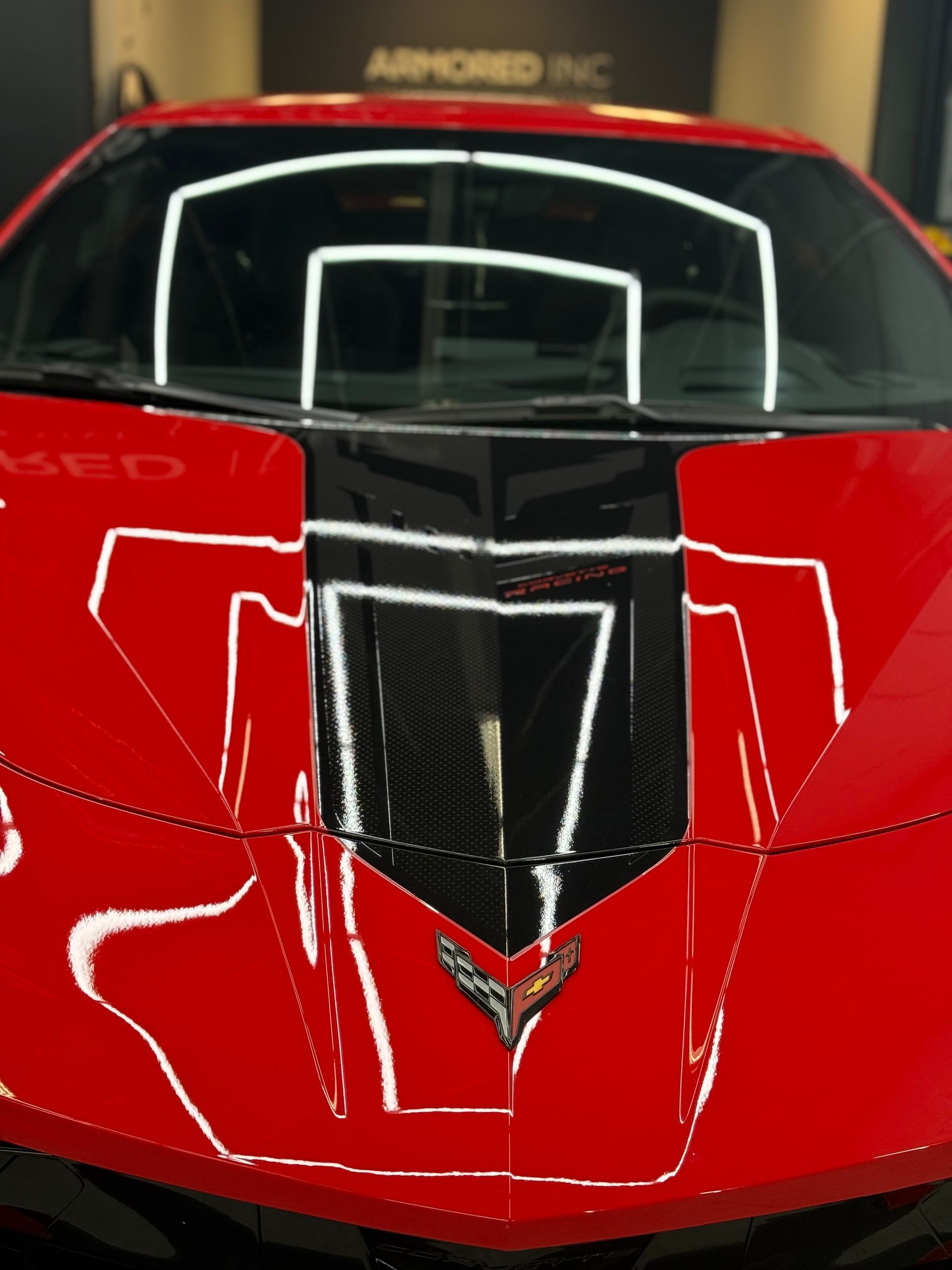 The front hood of a bright red Chevrolet Corvette with a black center stripe and emblem, parked in an indoor garage.