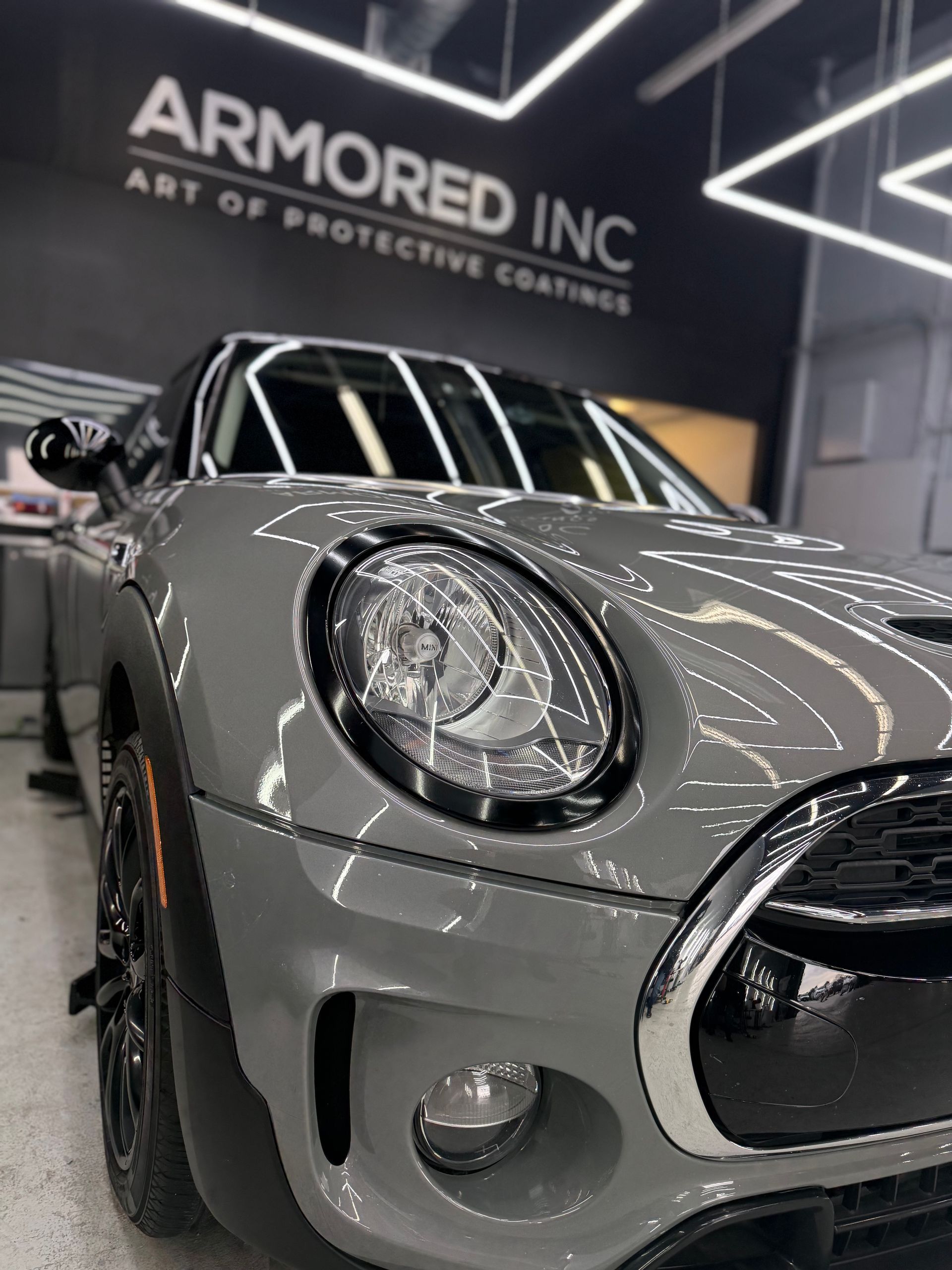 A close-up, low-angle shot of a gray Mini Cooper parked in a garage with 