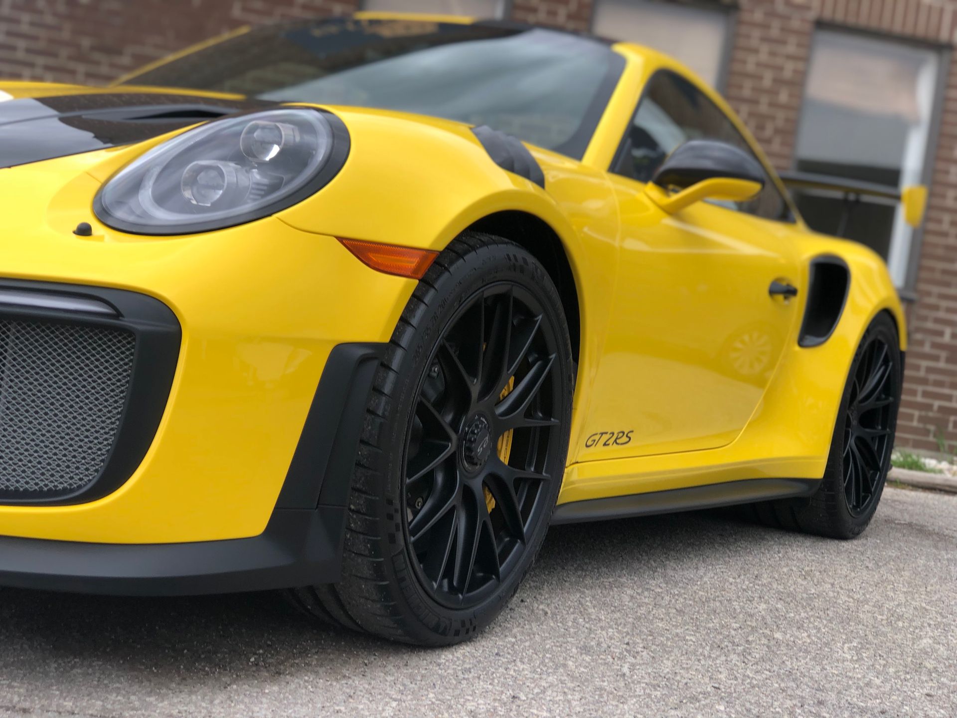 A vibrant yellow Porsche 911 GT3 RS parked on asphalt in front of a brick building.