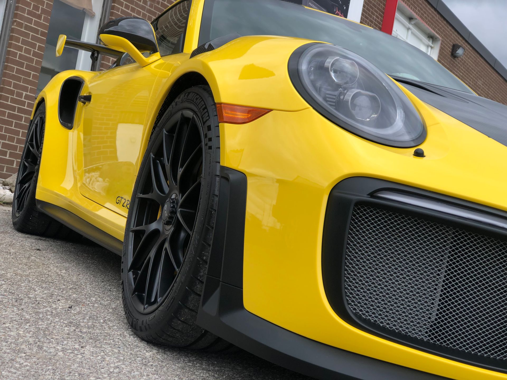 Low-angle, close-up shot of a bright yellow Porsche 911 GT2 RS parked on pavement outside a brick building.