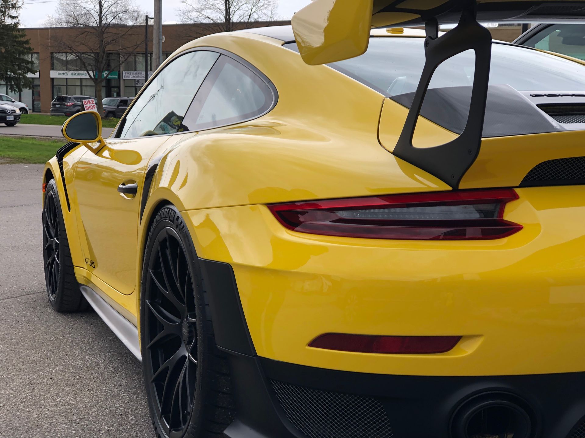 A bright yellow Porsche 911 GT3 RS with a large black rear wing, parked on an asphalt surface.