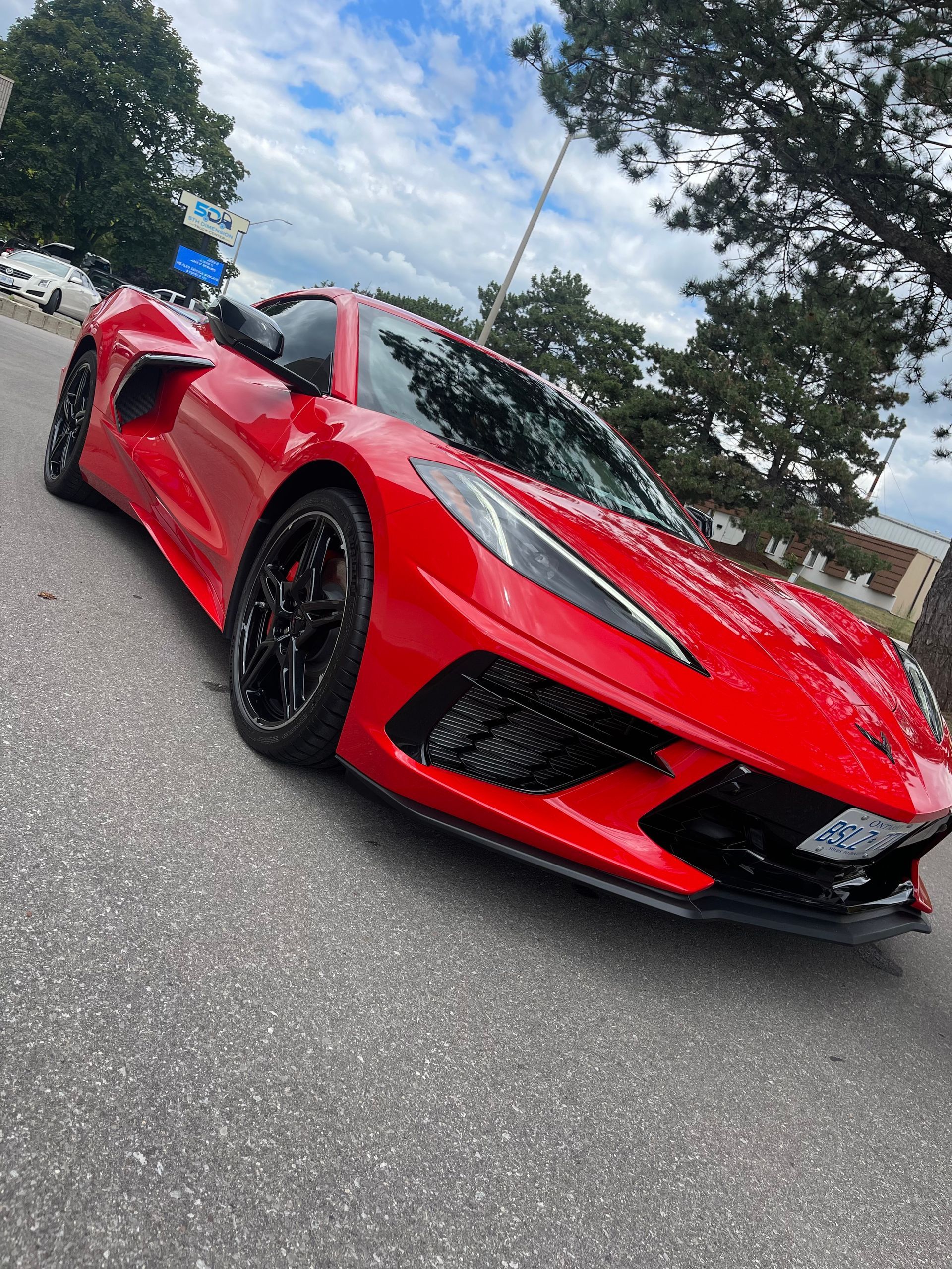 A bright red Chevrolet Corvette C8 parked on an asphalt surface under a cloudy sky.