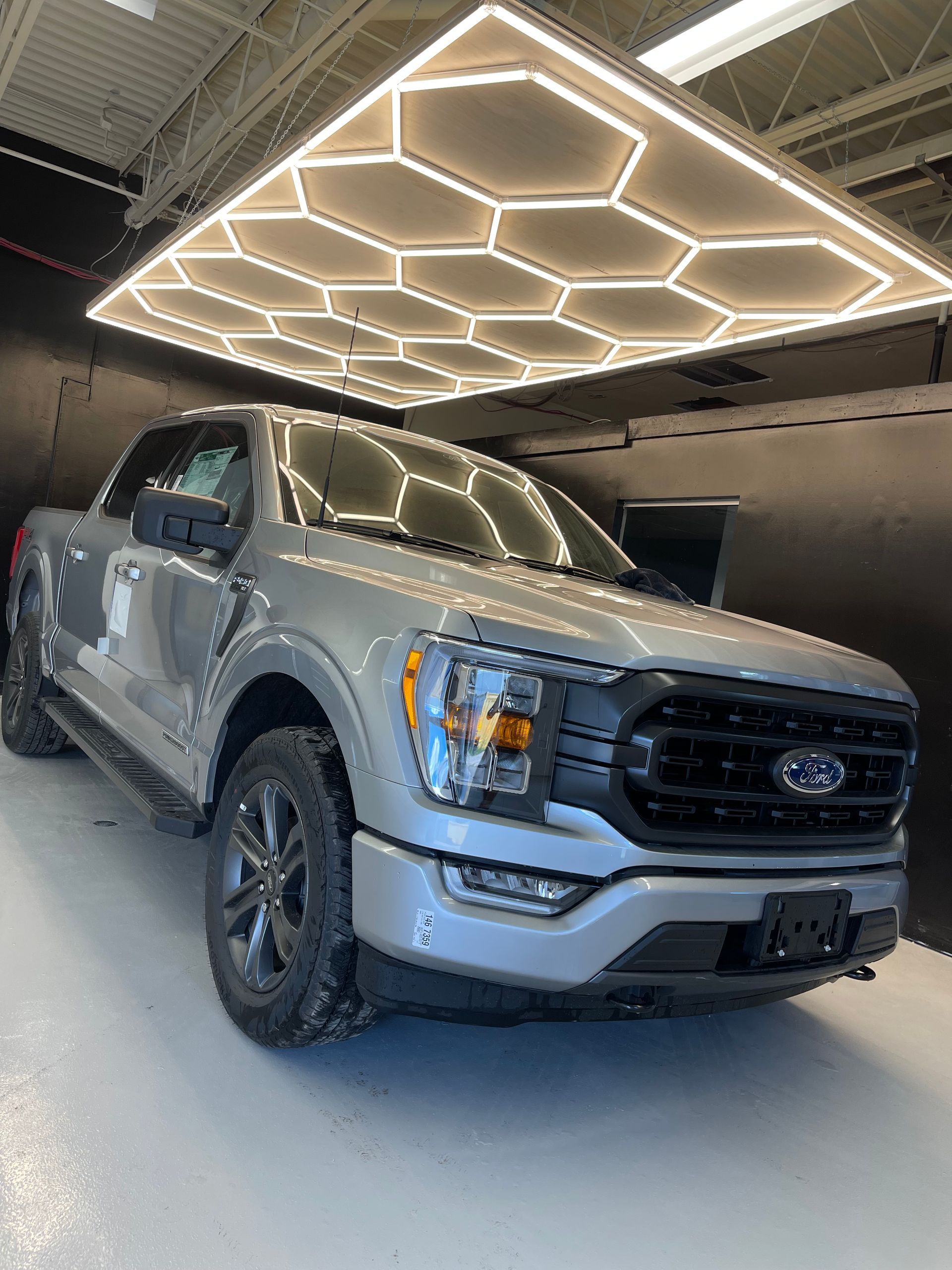 A silver Ford F-150 truck parked in a well-lit indoor space featuring a geometric, honeycomb-style ceiling light panel.