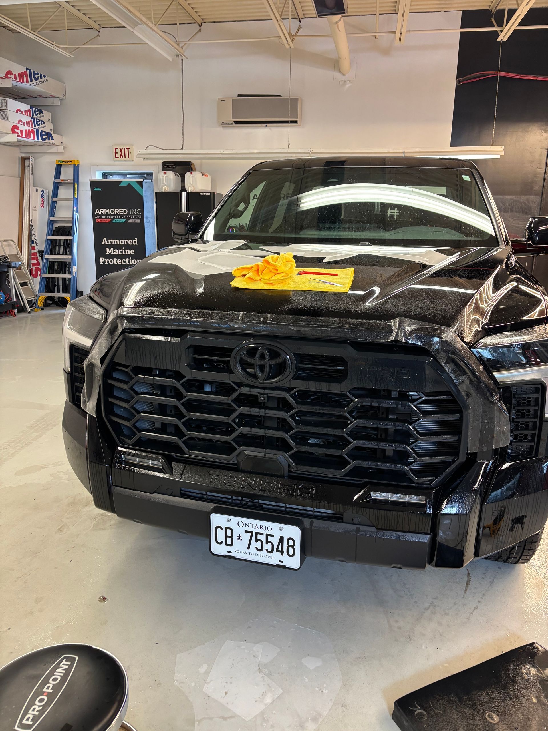 A black Toyota Tundra parked inside a shop with a yellow cloth on its hood and a Texas license plate visible.