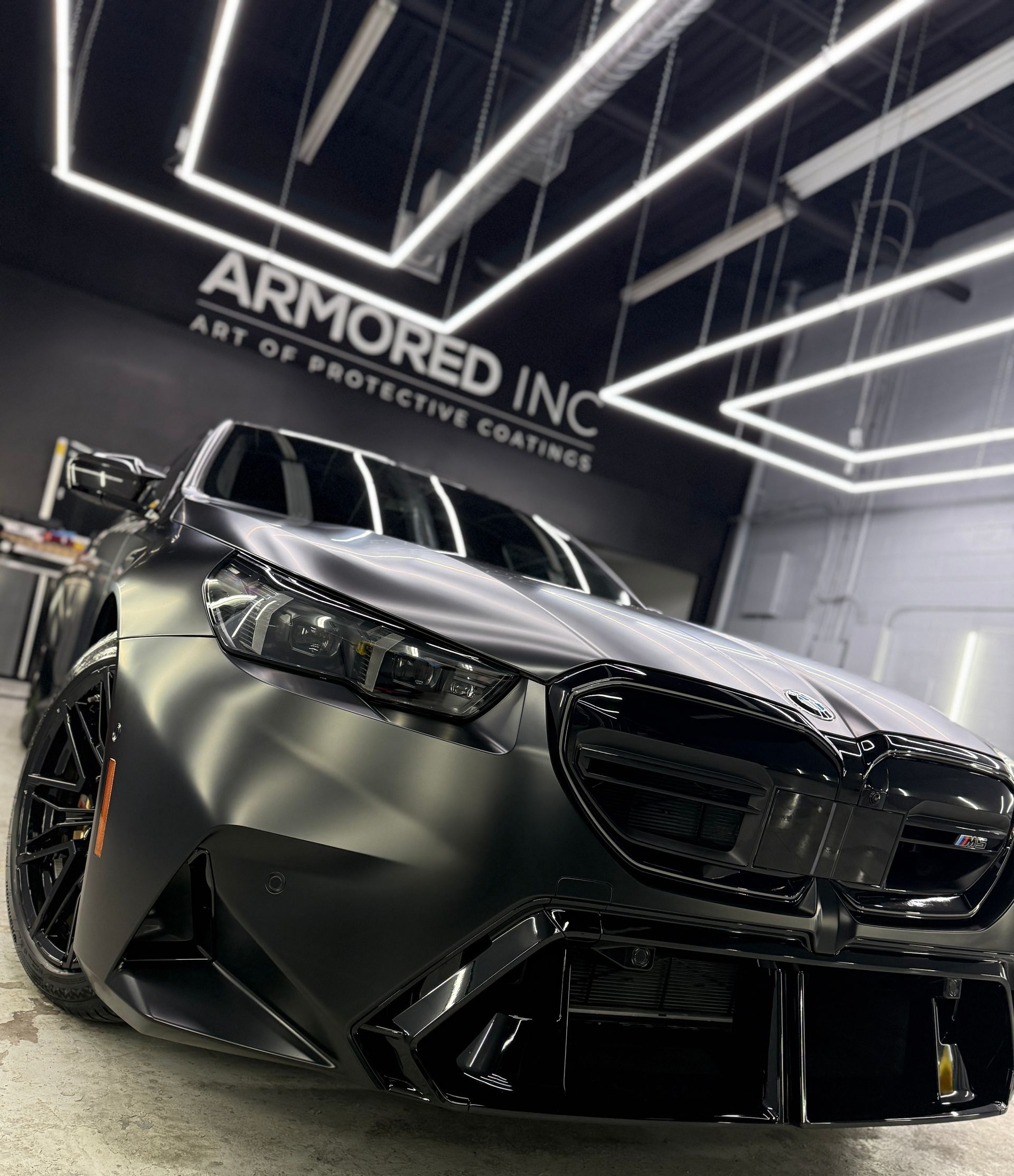 A matte black BMW parked inside a professional garage with modern overhead lighting and 
