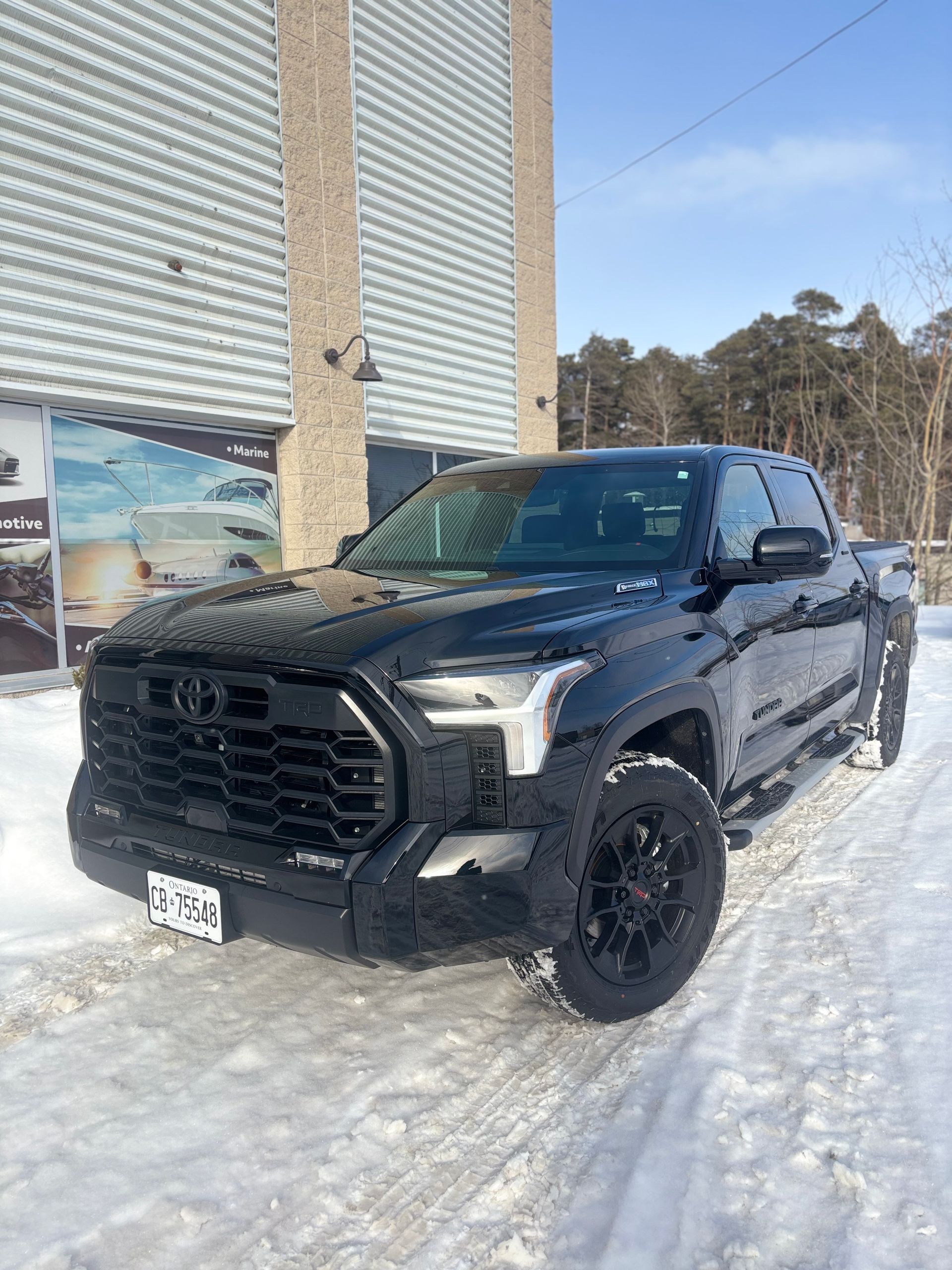 A black Toyota Tundra pickup truck parked on a snowy surface in front of a building with light-colored metal siding.