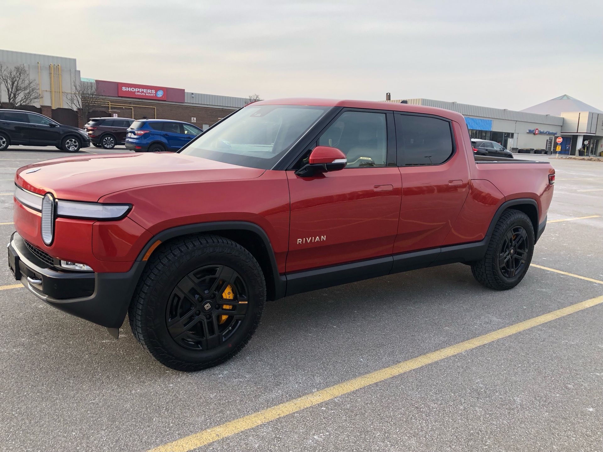 Red Rivian R1T electric pickup truck parked in a sunny, paved parking lot.