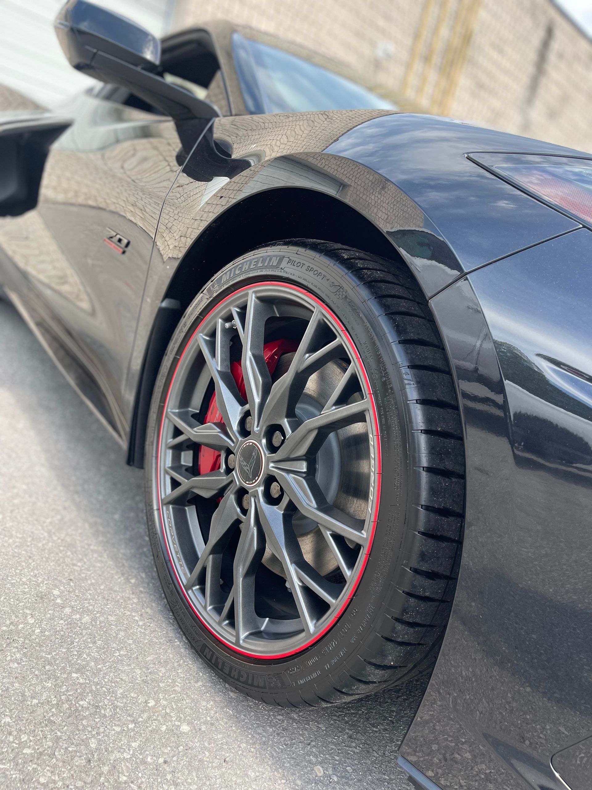 Close-up of a black sports car's front tire and grey multi-spoke wheel with a red rim accent and red brake calipers.