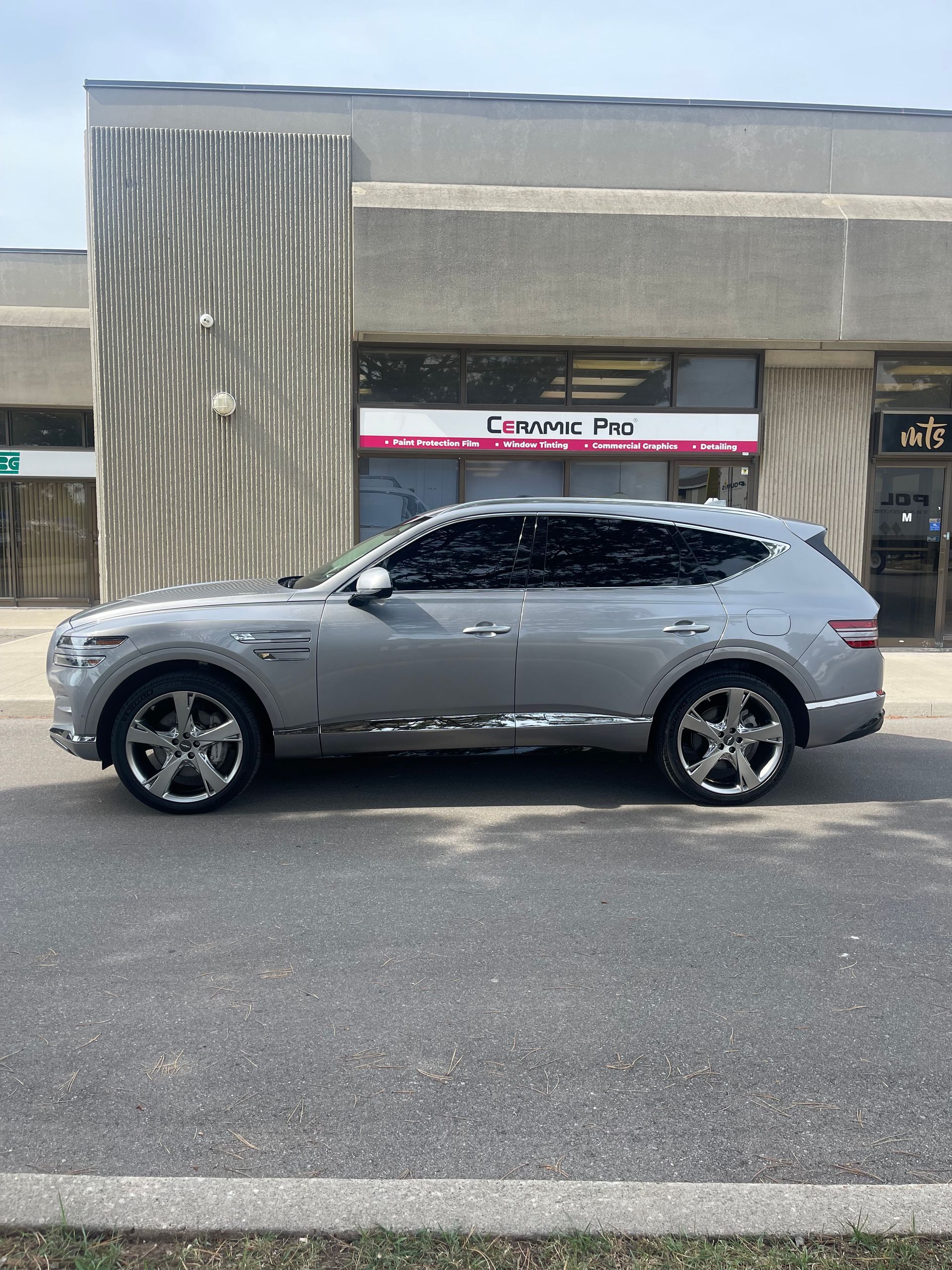 A side view of a silver SUV parked in front of a storefront with a 