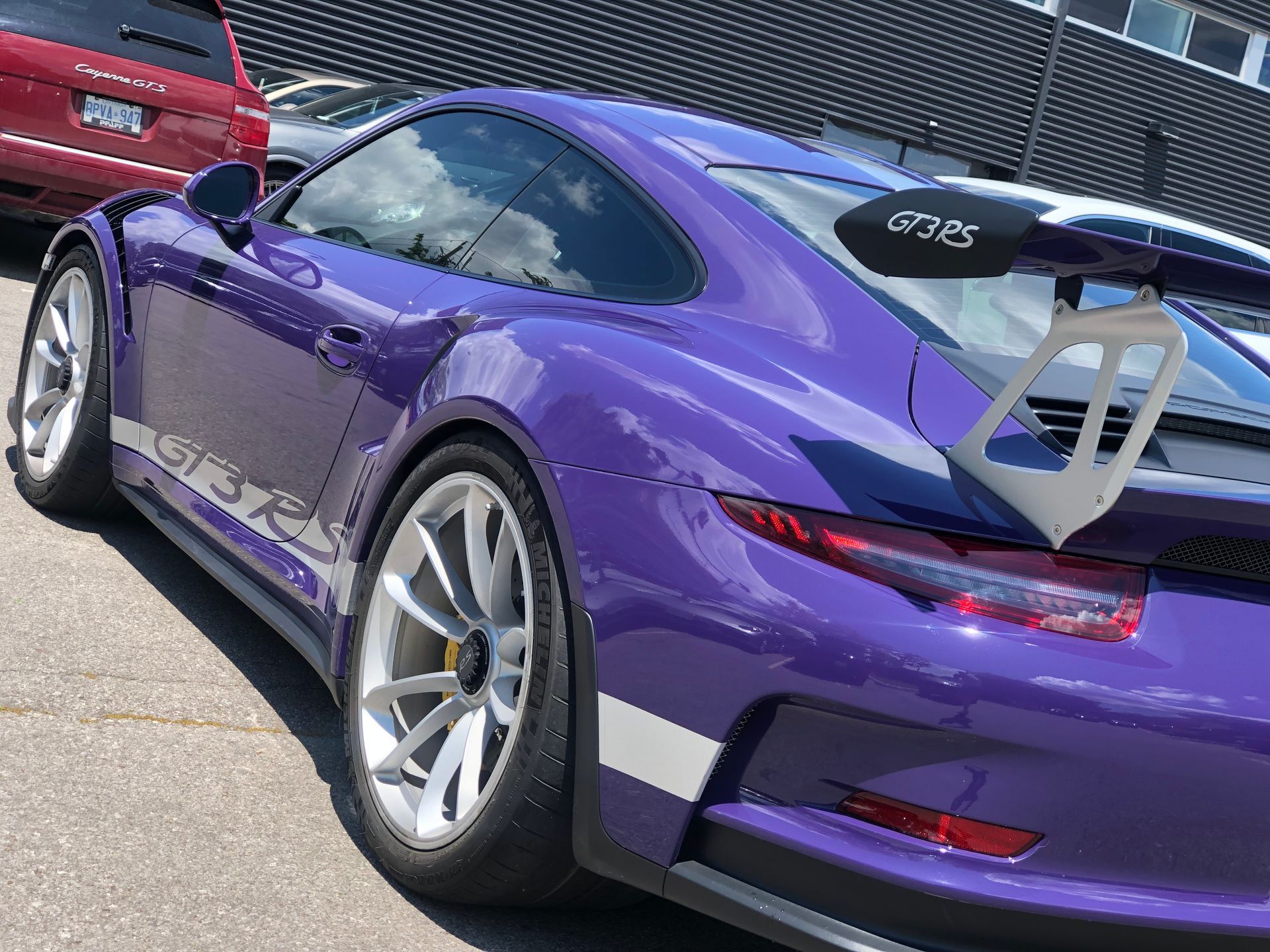 A purple Porsche 911 GT3 RS with silver wheels and a large rear spoiler parked in a sunny outdoor lot.
