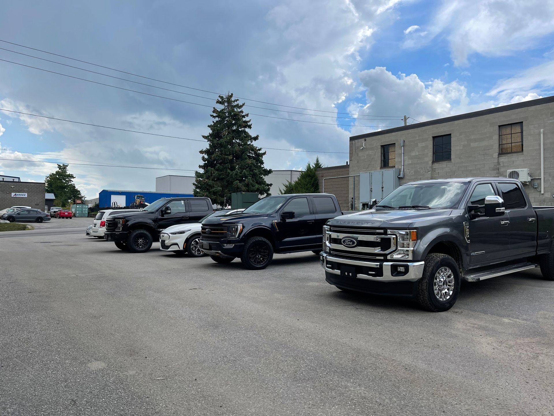 Three pickup trucks are parked in an outdoor gravel lot under a cloudy, blue sky.