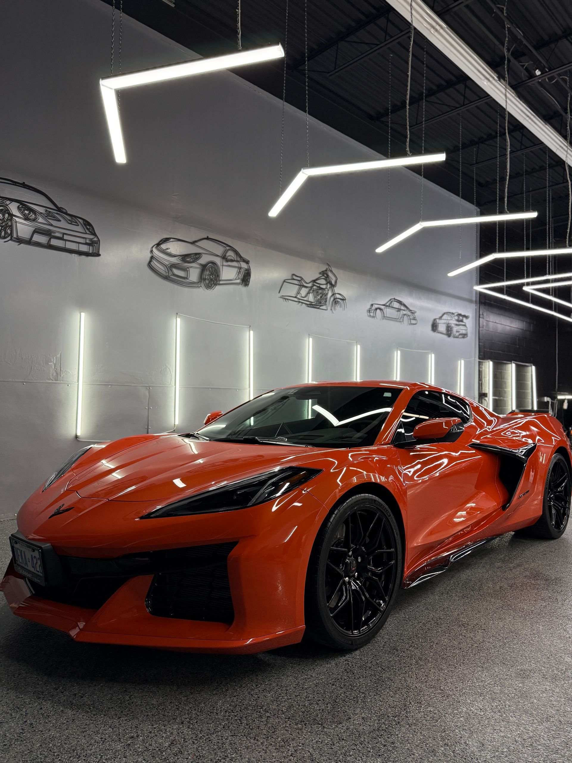 An orange sports car parked in a modern garage with neon lighting and car sketches on the wall.