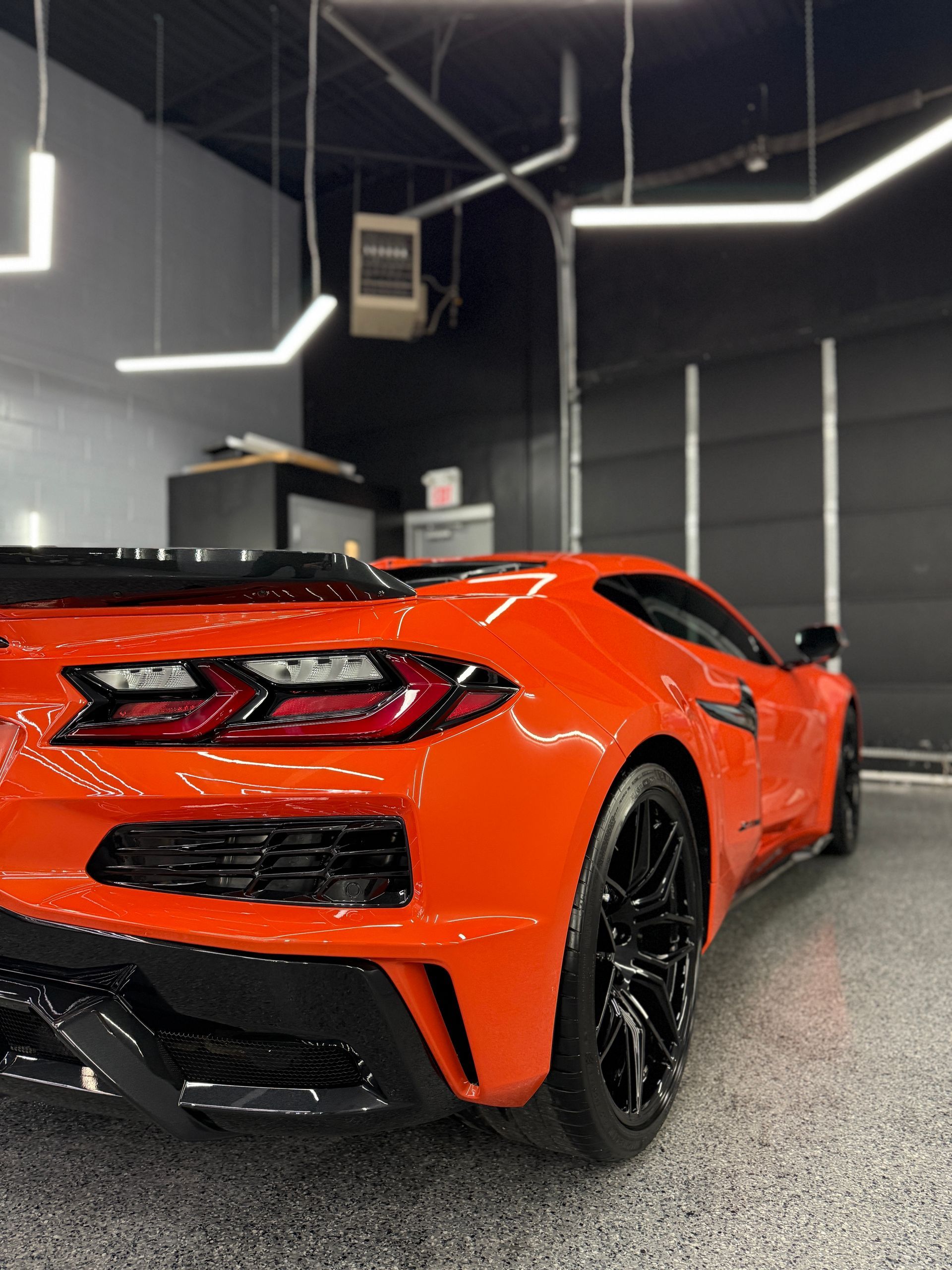 Bright orange Chevrolet Corvette parked inside a clean, modern garage with overhead lighting.