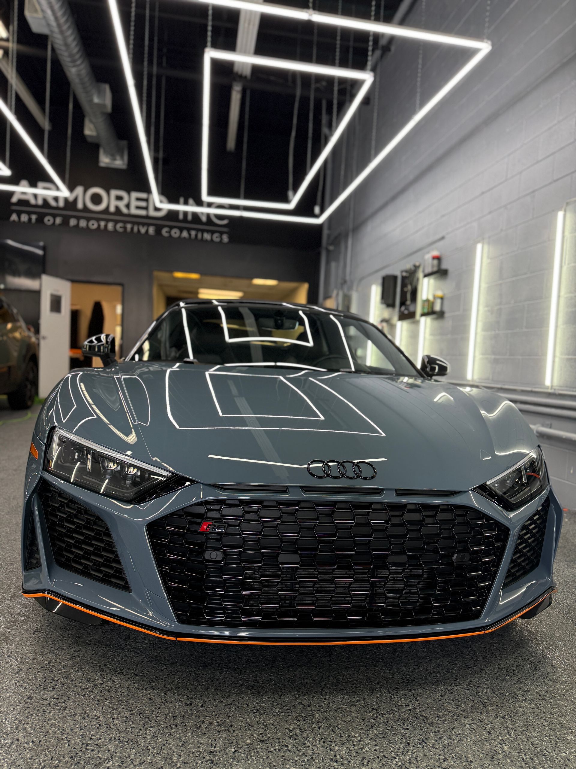 A grey Audi R8 sports car parked inside a well-lit, professional garage with 
